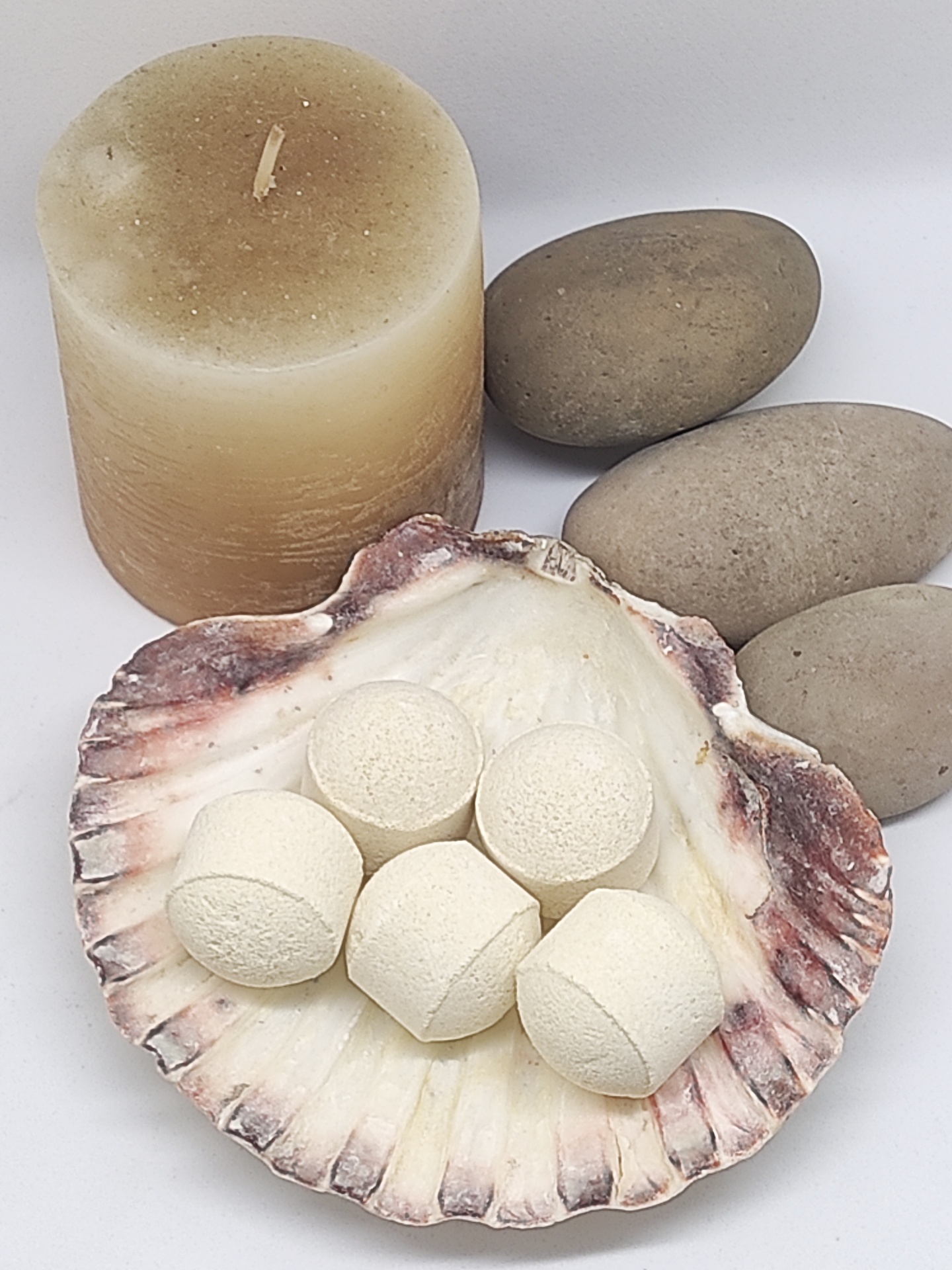 Vela bege, pedras cinzentas e concha com bolas brancas sobre fundo branco