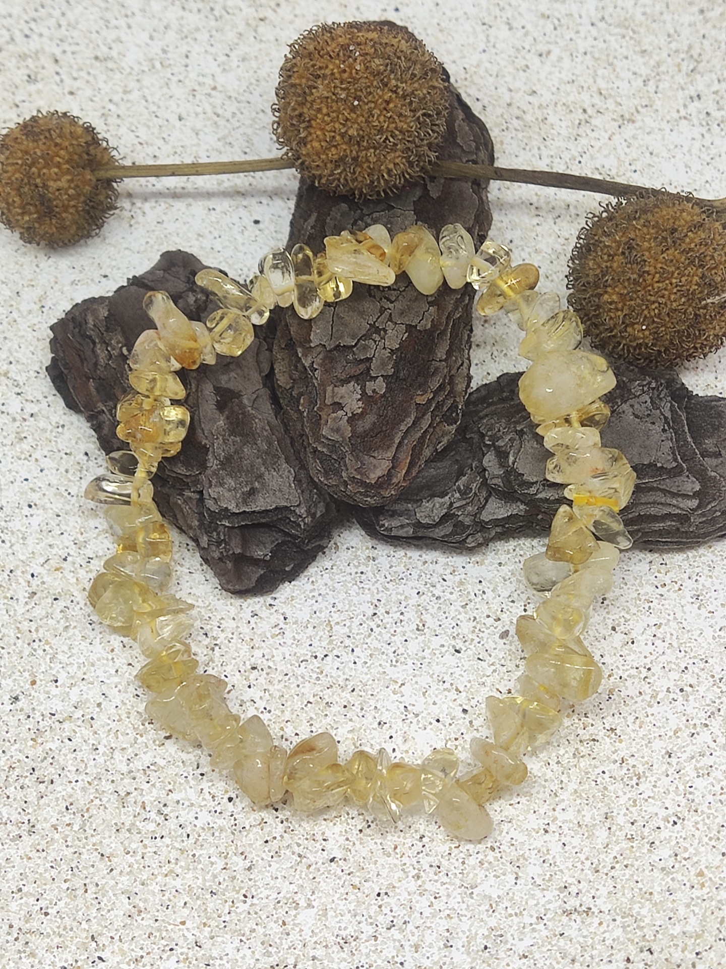 Pulseira de pedras de citrino amarelo sobre fundo claro com madeira escura e bolas secas de plantas