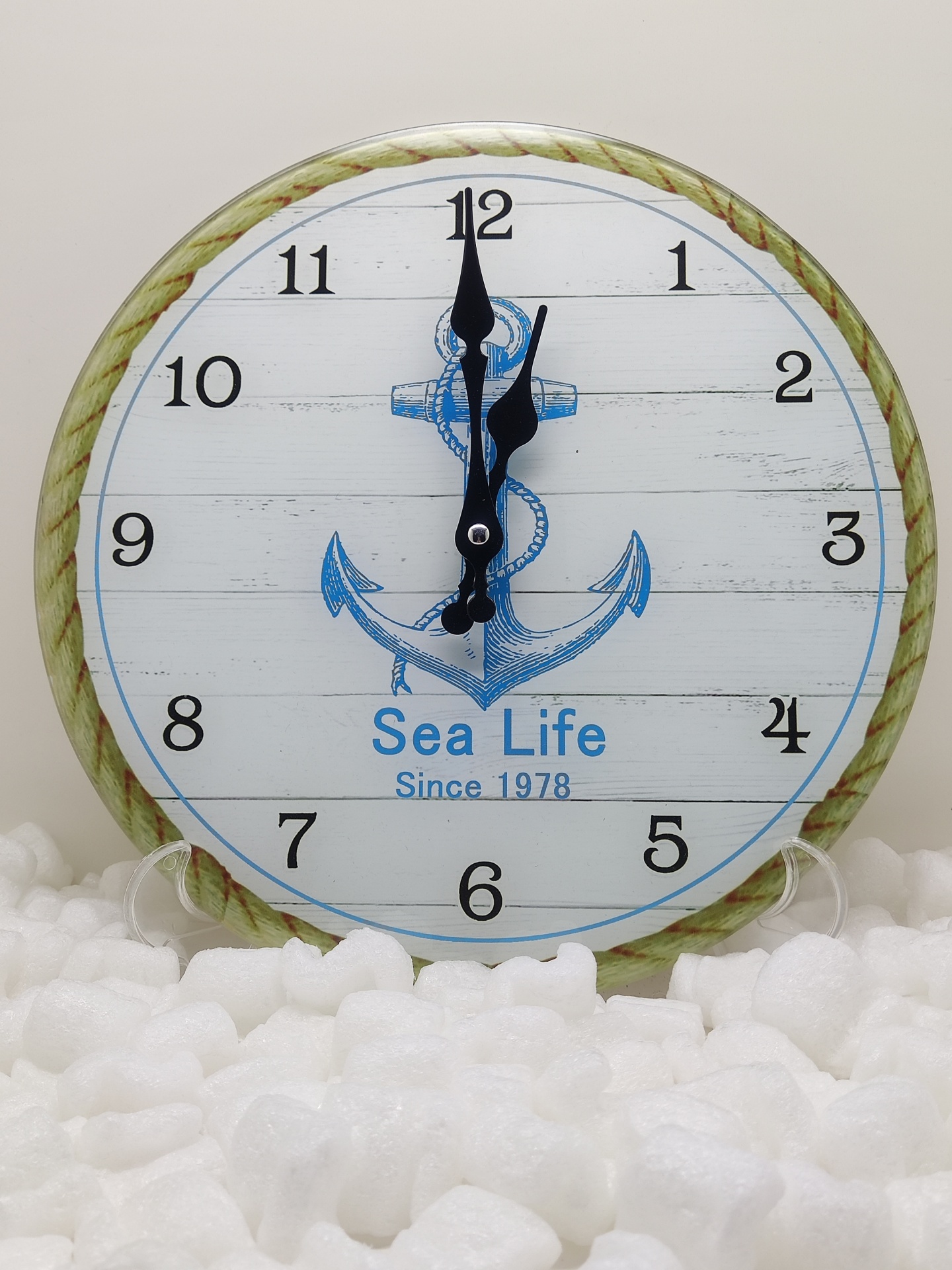 Relógio redondo com âncora azul e texto Sea Life Since 1978 sobre superfície de plástico bolha