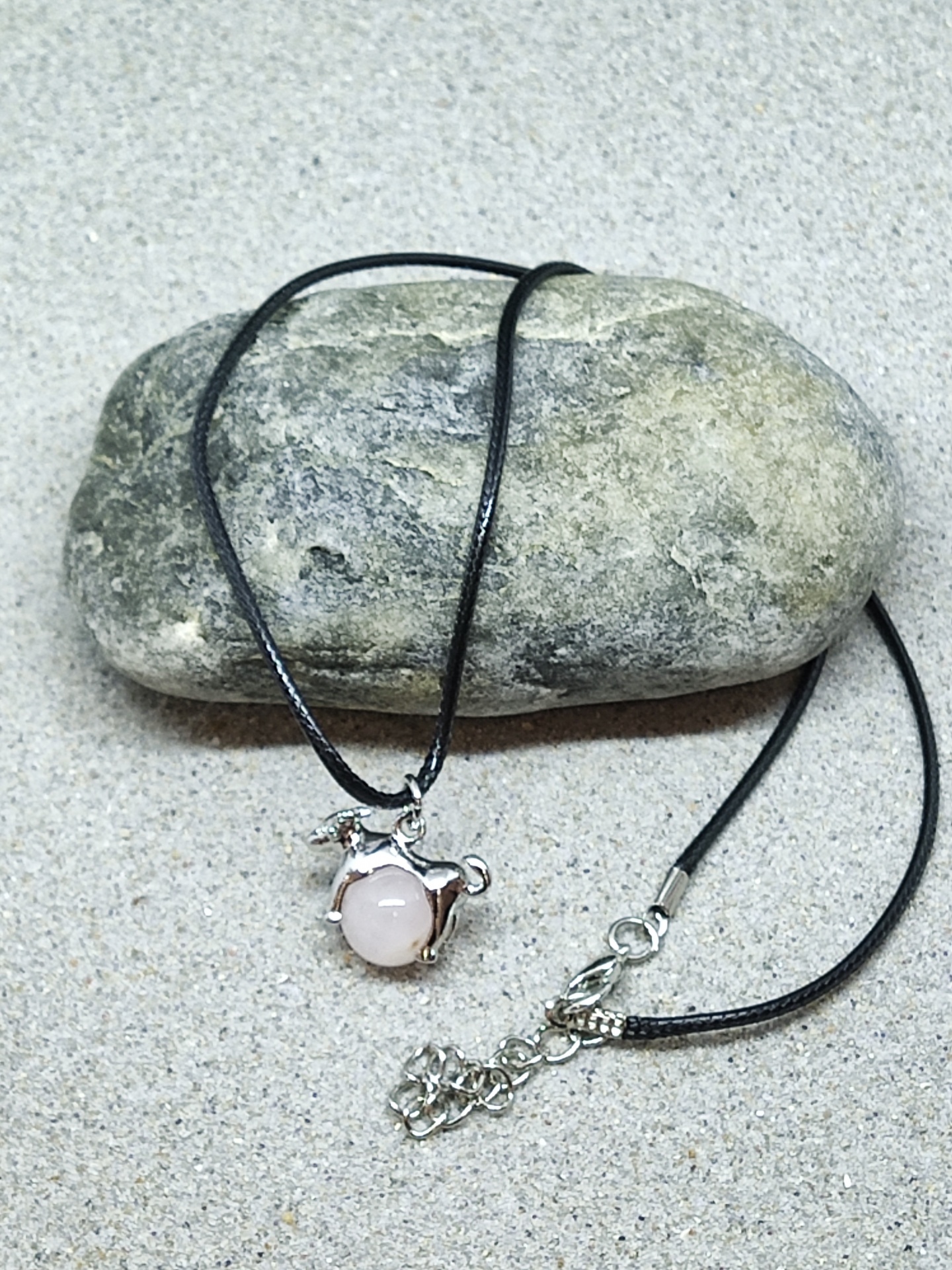 Colar com pendente de pedra rosa e estrutura metálica prateada sobre pedra cinza