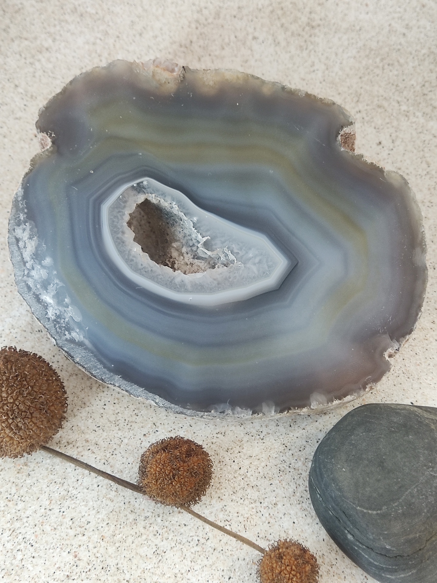 Fatias de ágata cinza e azul com flores secas e pedra cinza sobre fundo claro