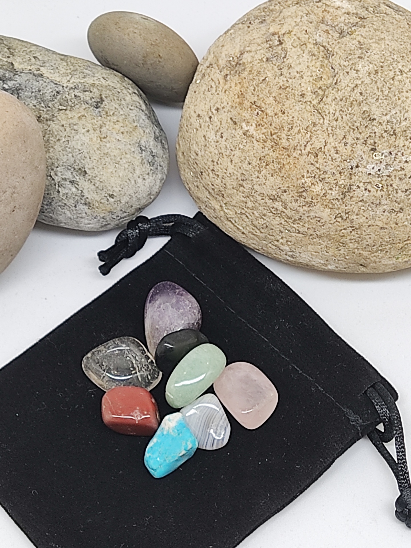 Pedras polidas coloridas sobre saco preto com pedras neutras no fundo