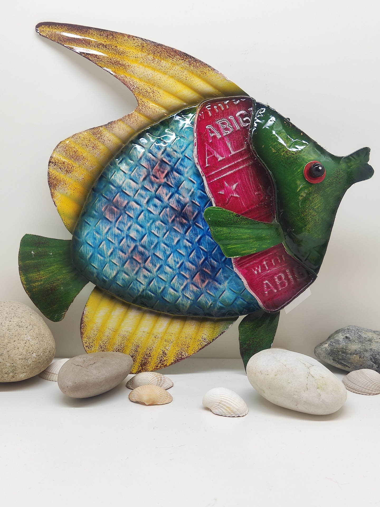 Peixe decorativo metálico colorido com pedras e conchas ao redor