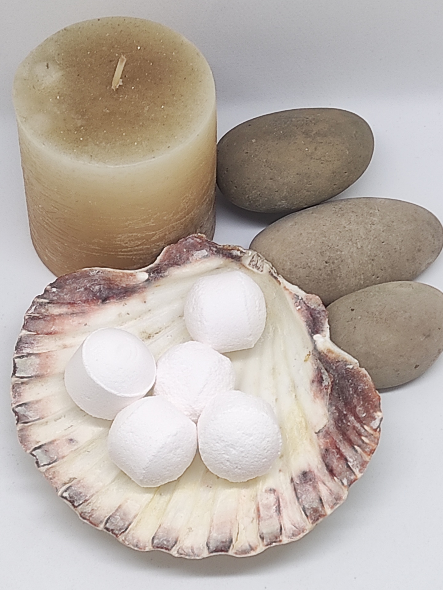 Vela beige cilíndrica, pedras cinzentas lisas, concha com bolas brancas