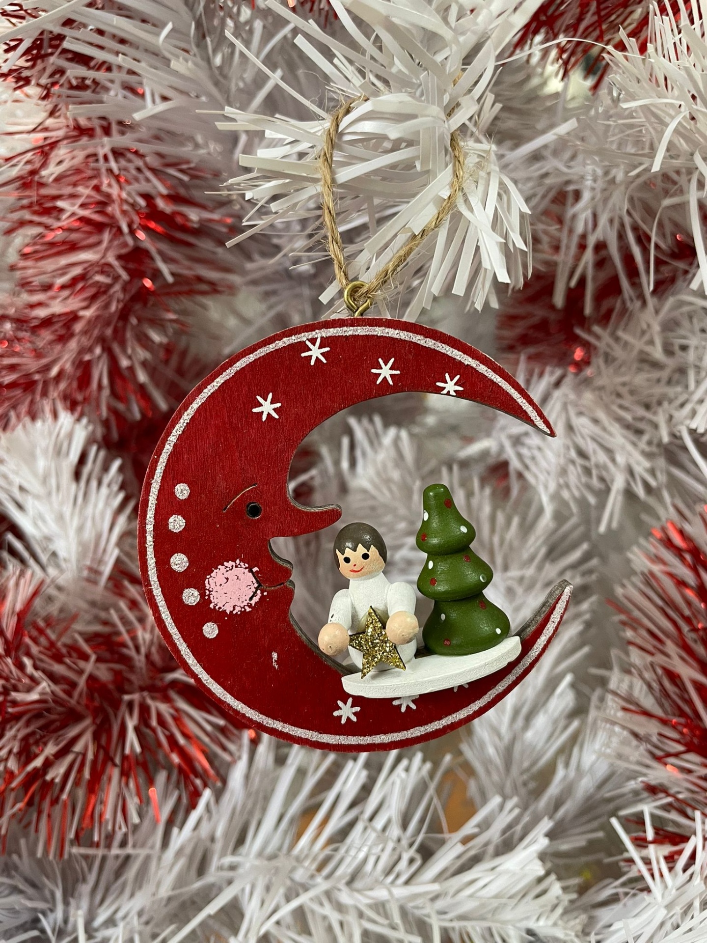 Enfeite de Natal lua vermelha, anjinho e árvore verde pendurado em árvore branca com detalhes vermelhos