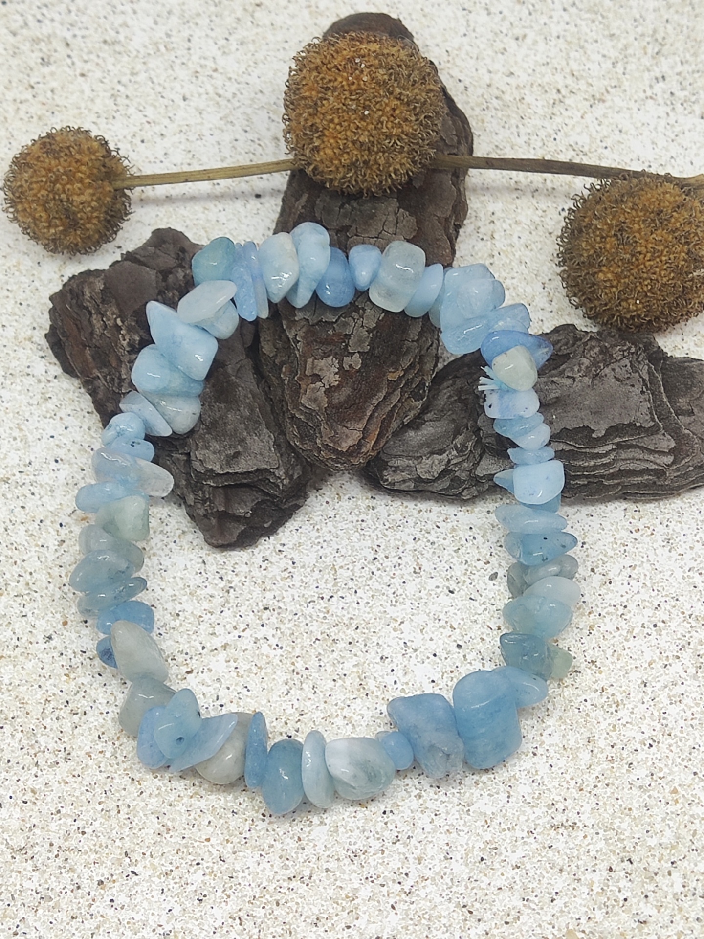 Pulseira de pedras azul-claro sobre casca de árvore e flores secas