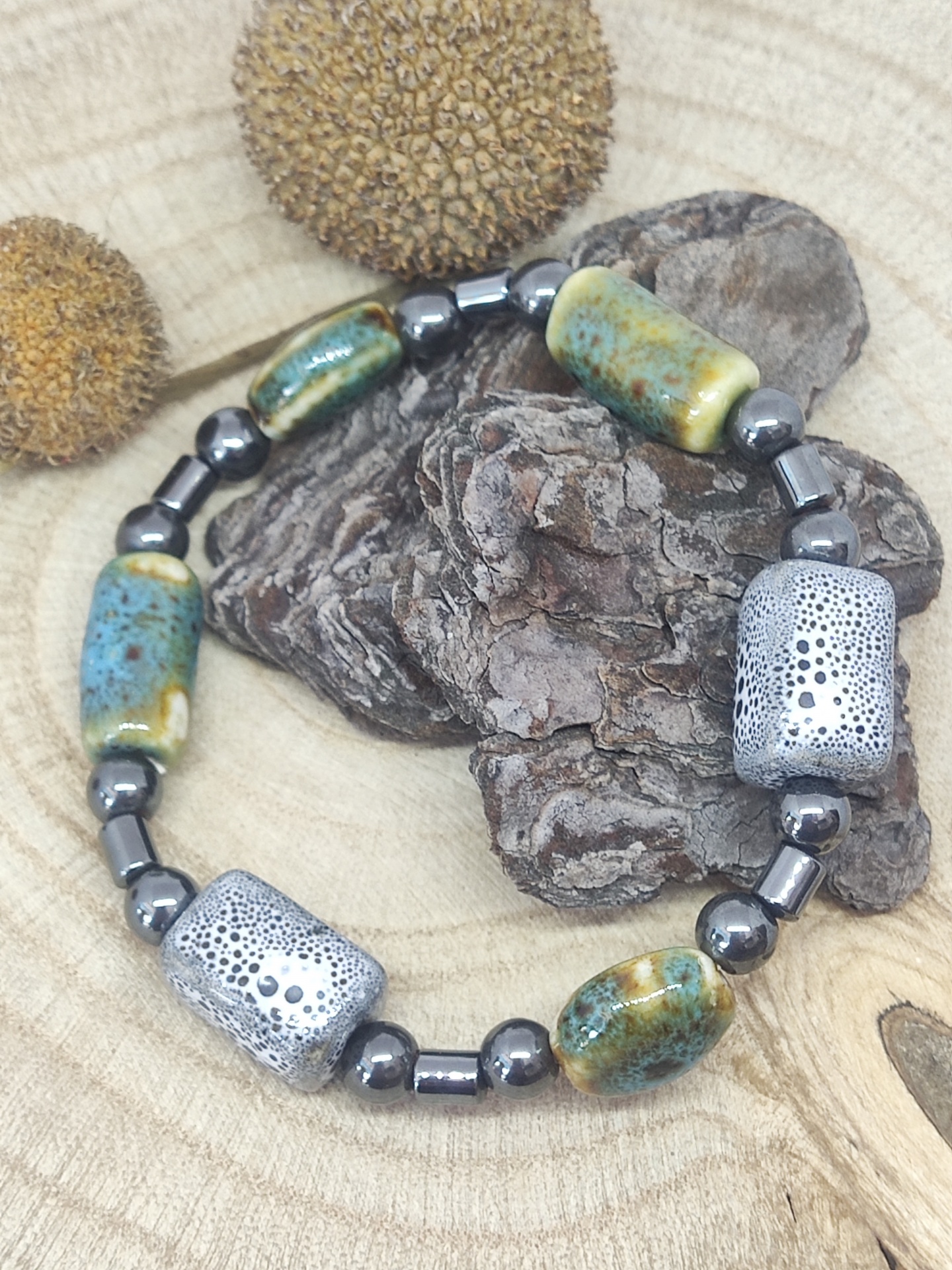Pulseira cerâmica azul e castanha com contas metálicas sobre casca e madeira
