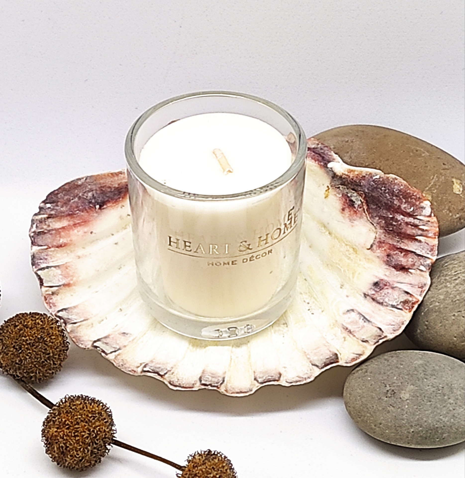 Vela em copo de vidro sobre concha decorativa com pedras e frutos secos