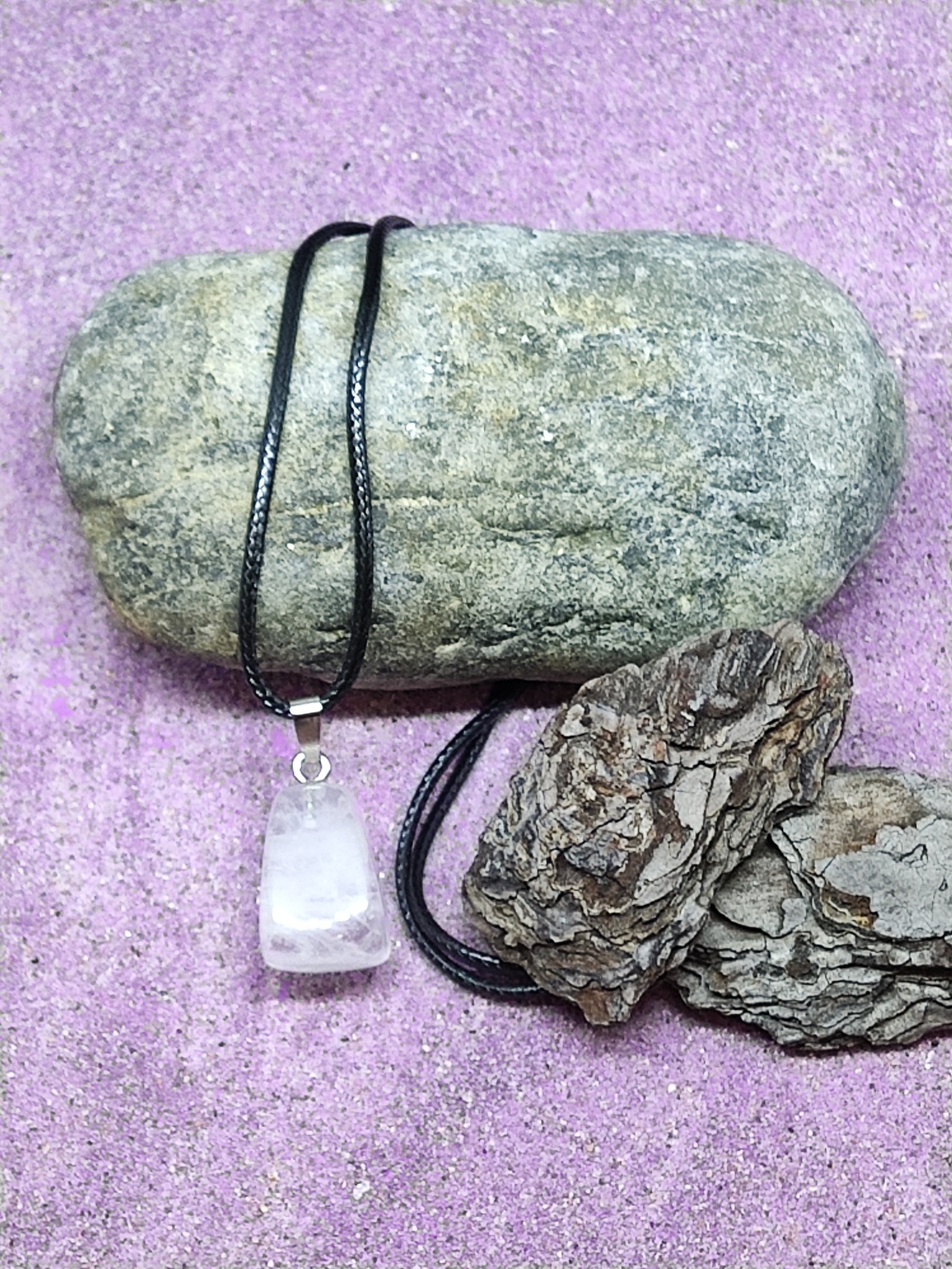 Colar com pendente de pedra branca e cordão preto sobre pedra cinzenta e fundo roxo