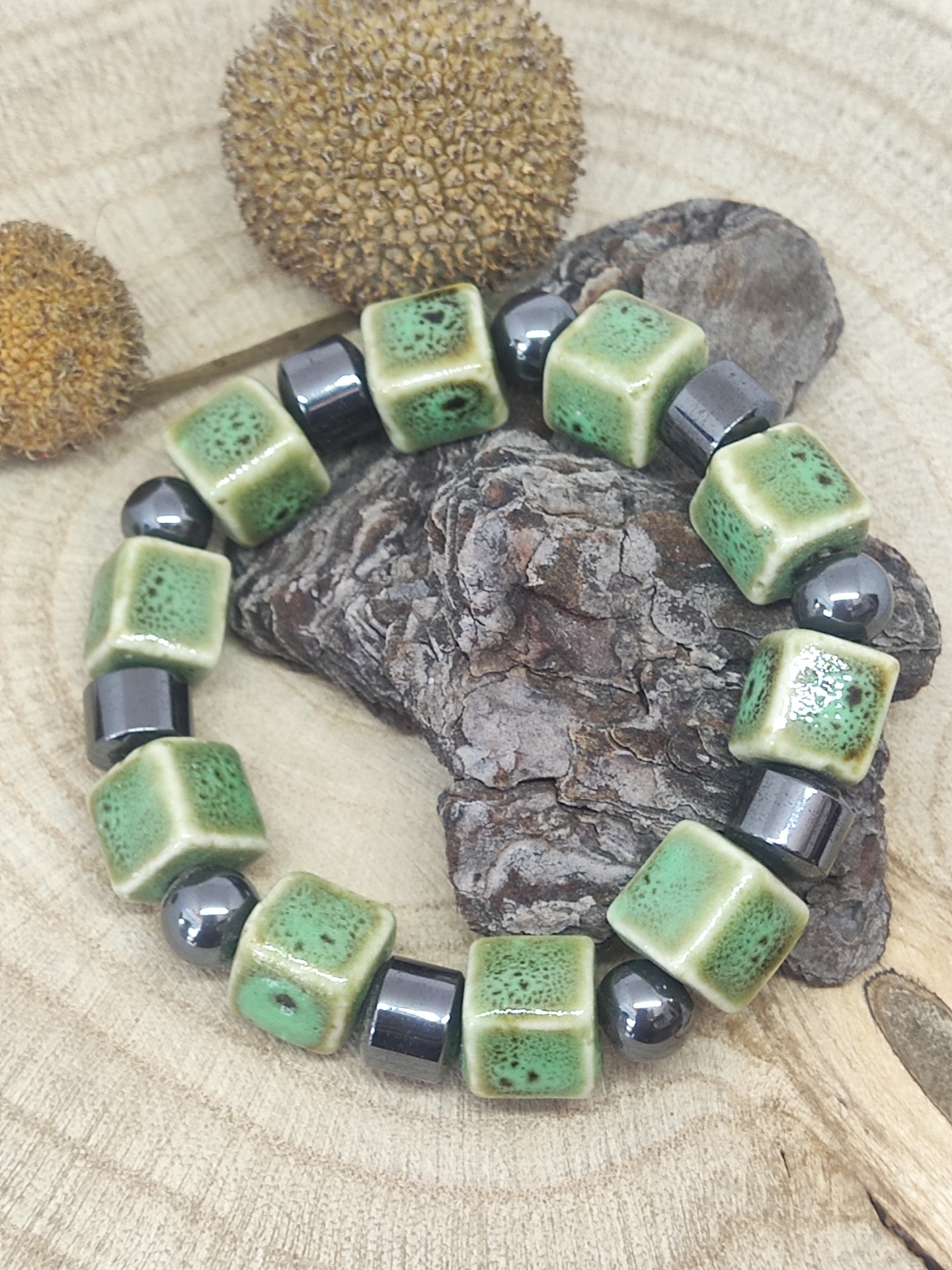 Pulseira com contas verdes de cerâmica e esferas metálicas sobre madeira clara