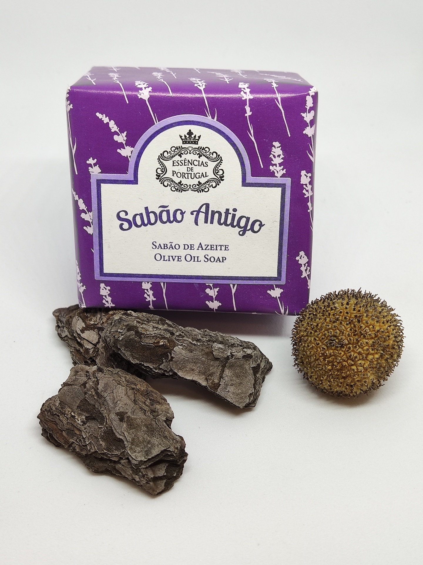Sabão em barra embalado em roxo e branco com casca de árvore e semente ao lado
