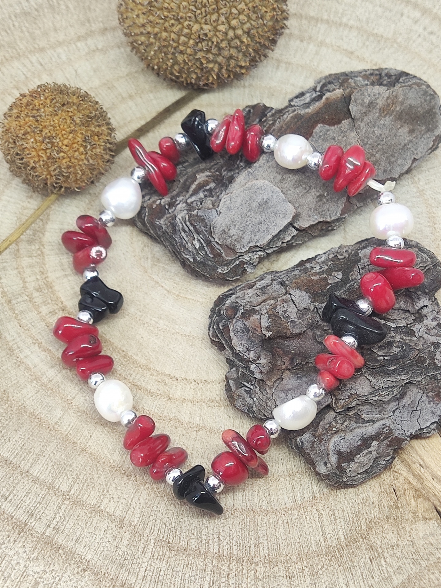 Pulseira com pedras vermelhas, negras e pérolas sobre madeira clara e casca de árvore