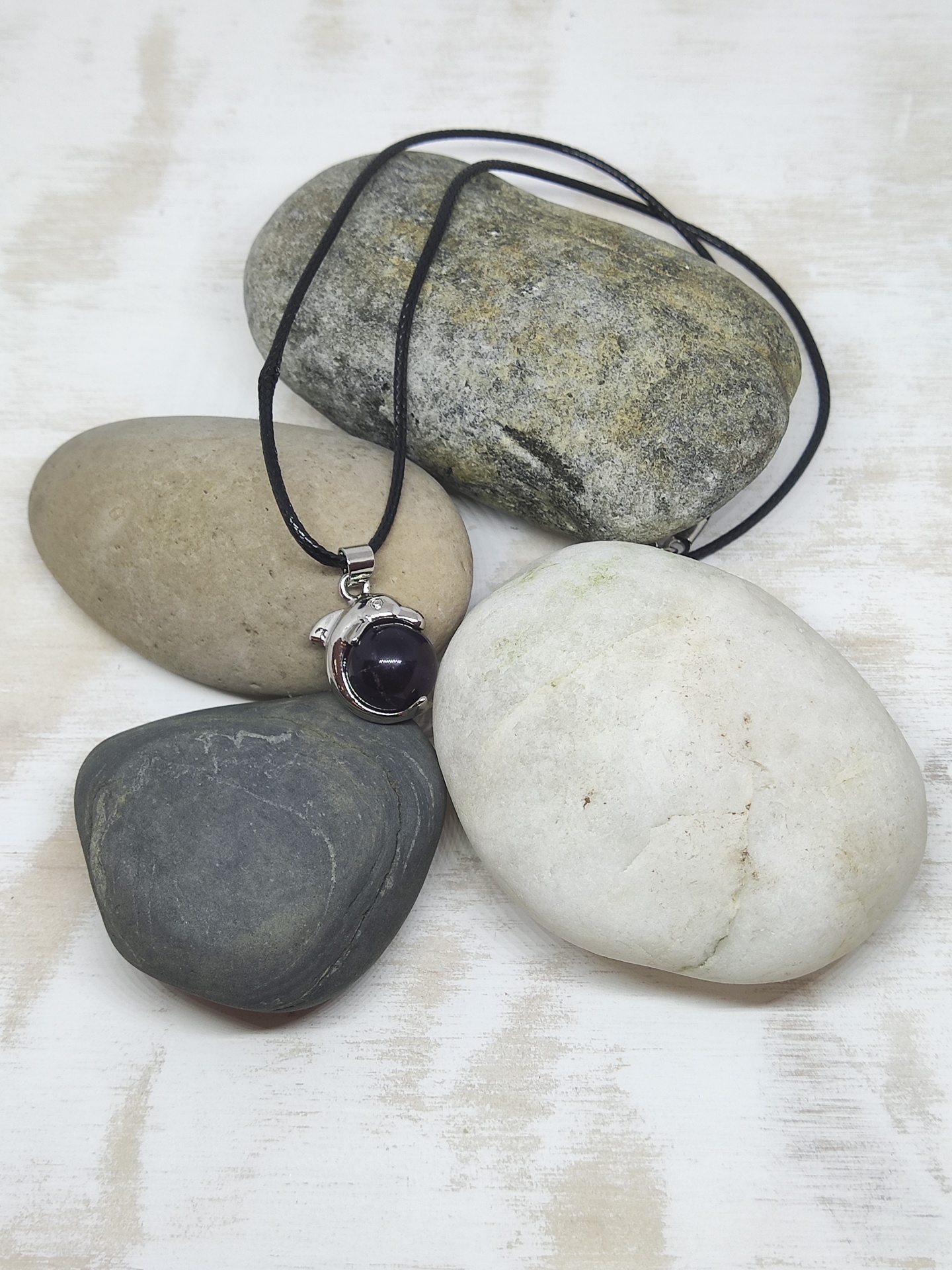 Colar com pendente em pedra preta sobre pedras lisas variadas em fundo branco.