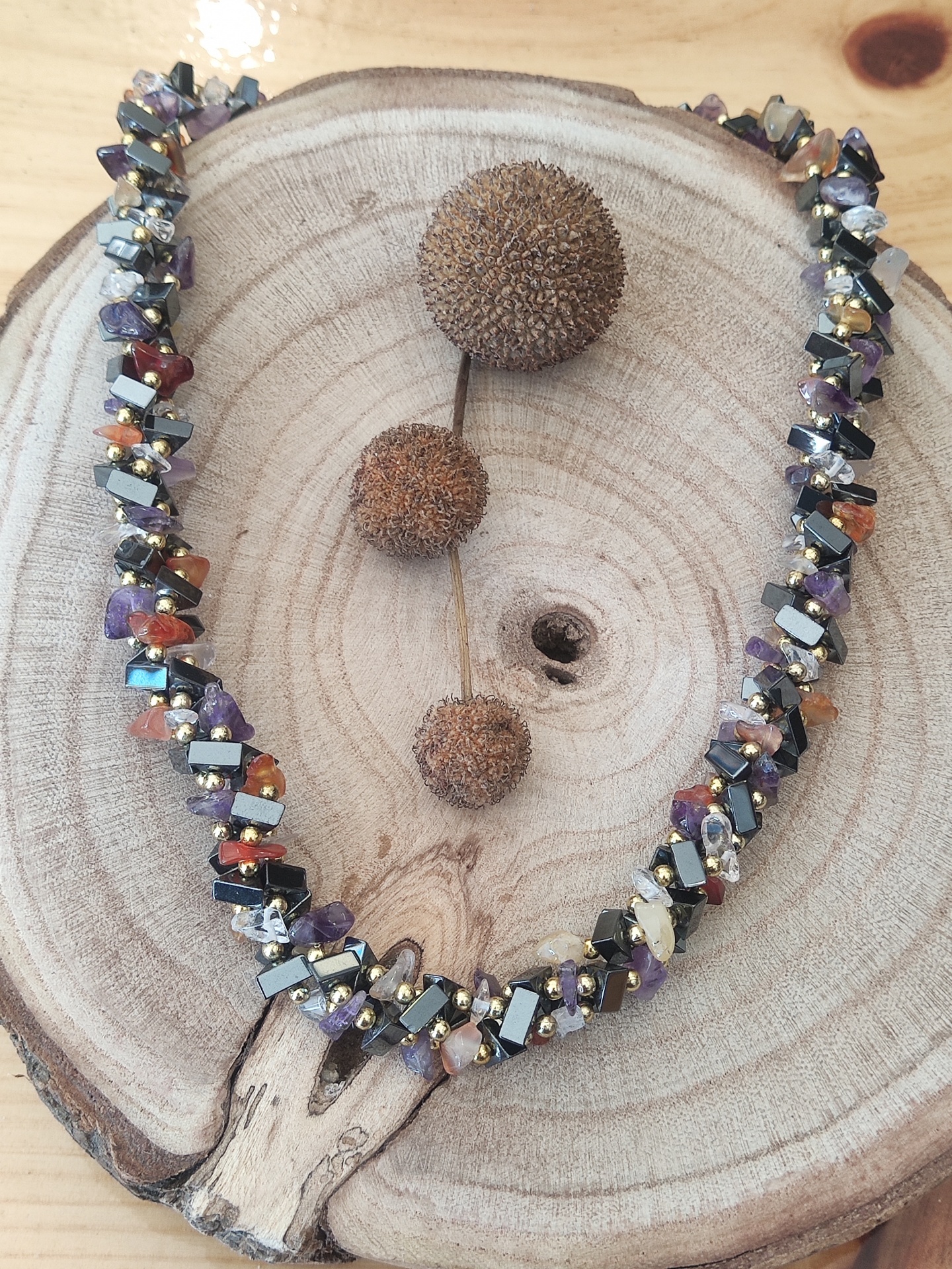 Colar de contas coloridas sobre base de madeira redonda com frutos secos