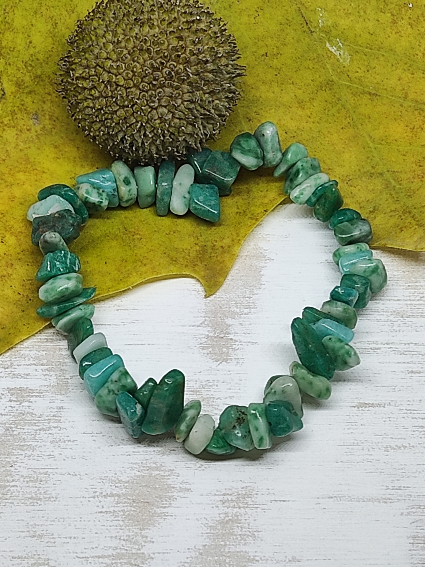 Pulseira de pedras verdes irregular sobre fundo amarelo e branco com objeto visual arredondado