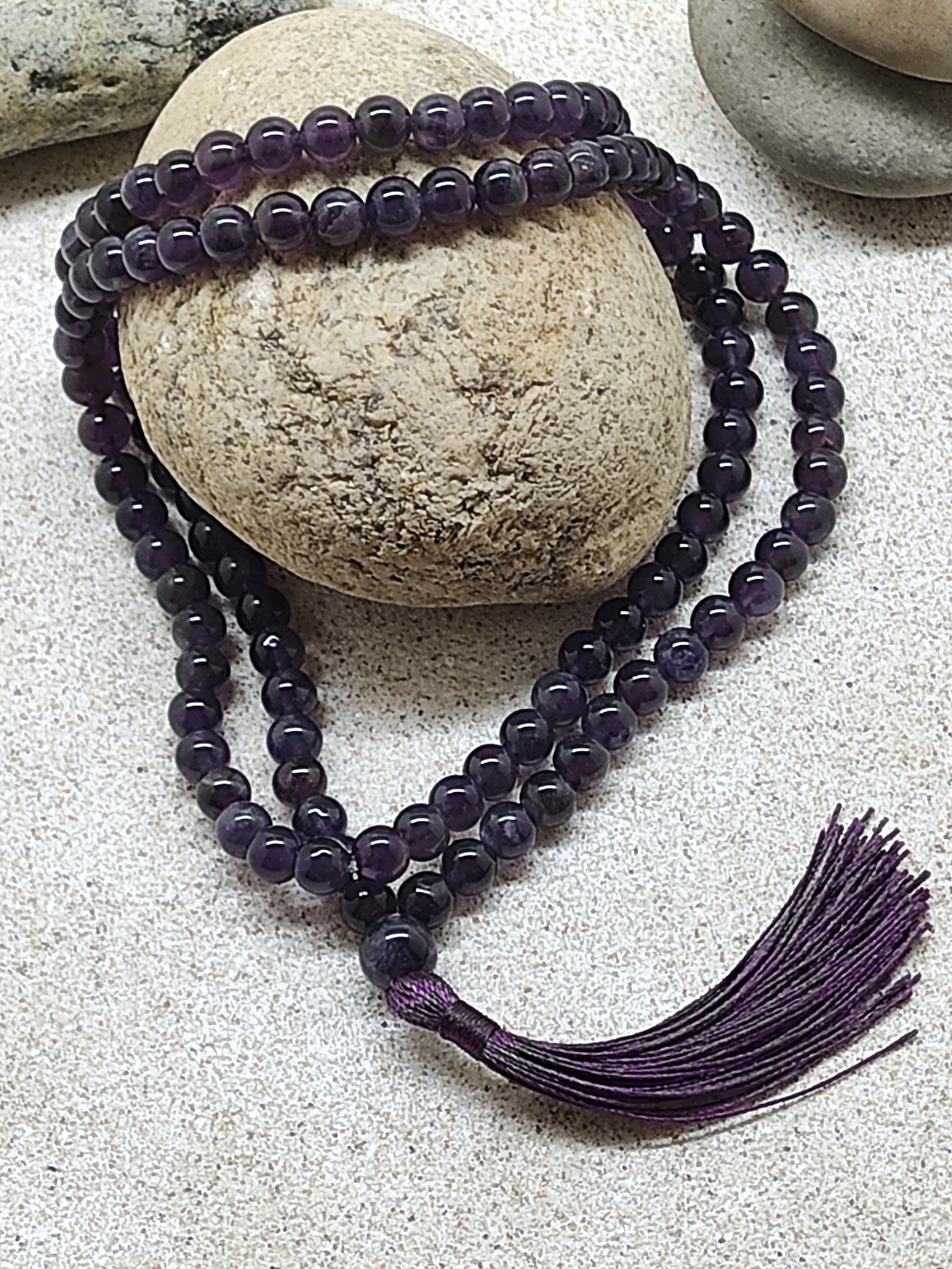 Colar de contas de ametista roxa com tassel sobre pedras e areia
