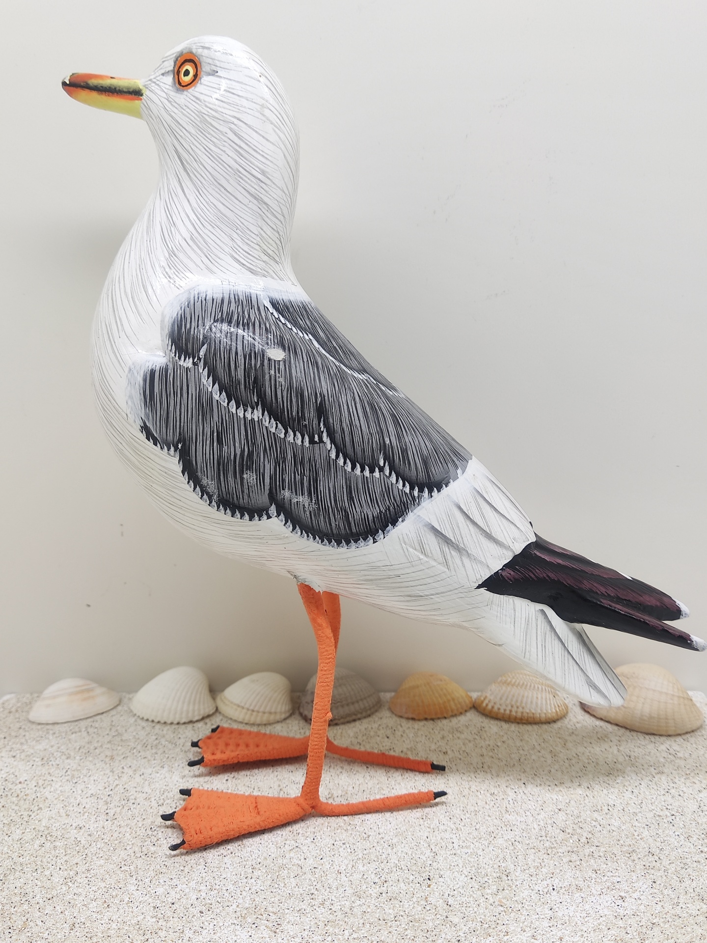 Figura decorativa de gaivota em madeira pintada sobre superfície com conchas