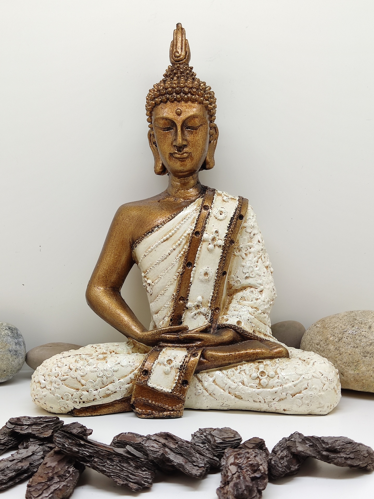 Estátua de Buda dourada e branca em meditação com pedras e madeira
