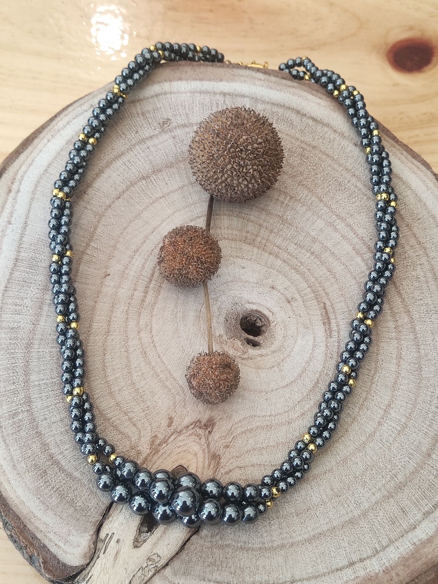 colar de contas metálicas cinzentas e douradas sobre base de madeira com bolas secas marrons