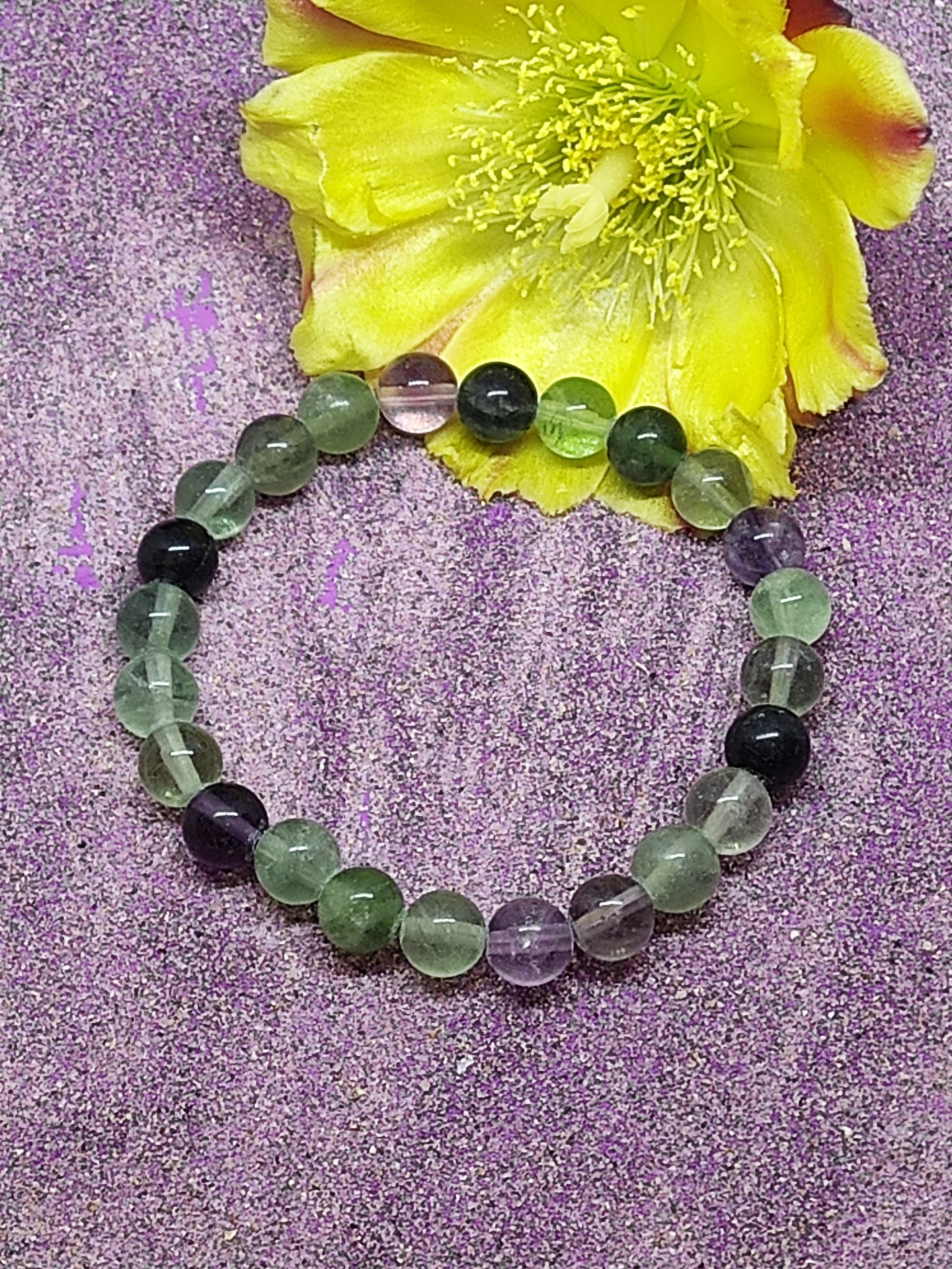 Pulseira de esferas coloridas e translúcidas, com flor amarela ao fundo