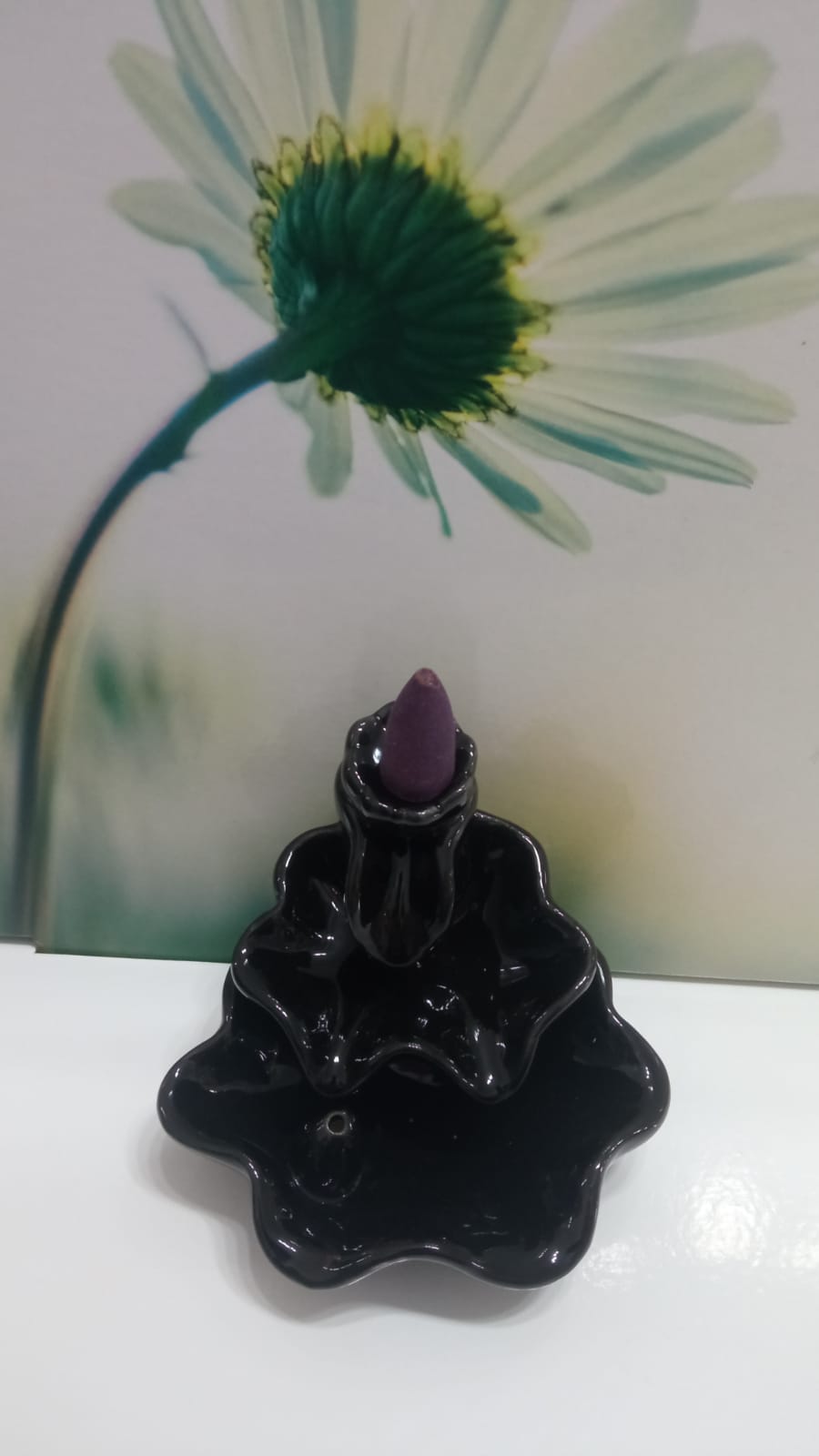 Suporte de incenso preto com cone roxo em frente a flor branca desfocada