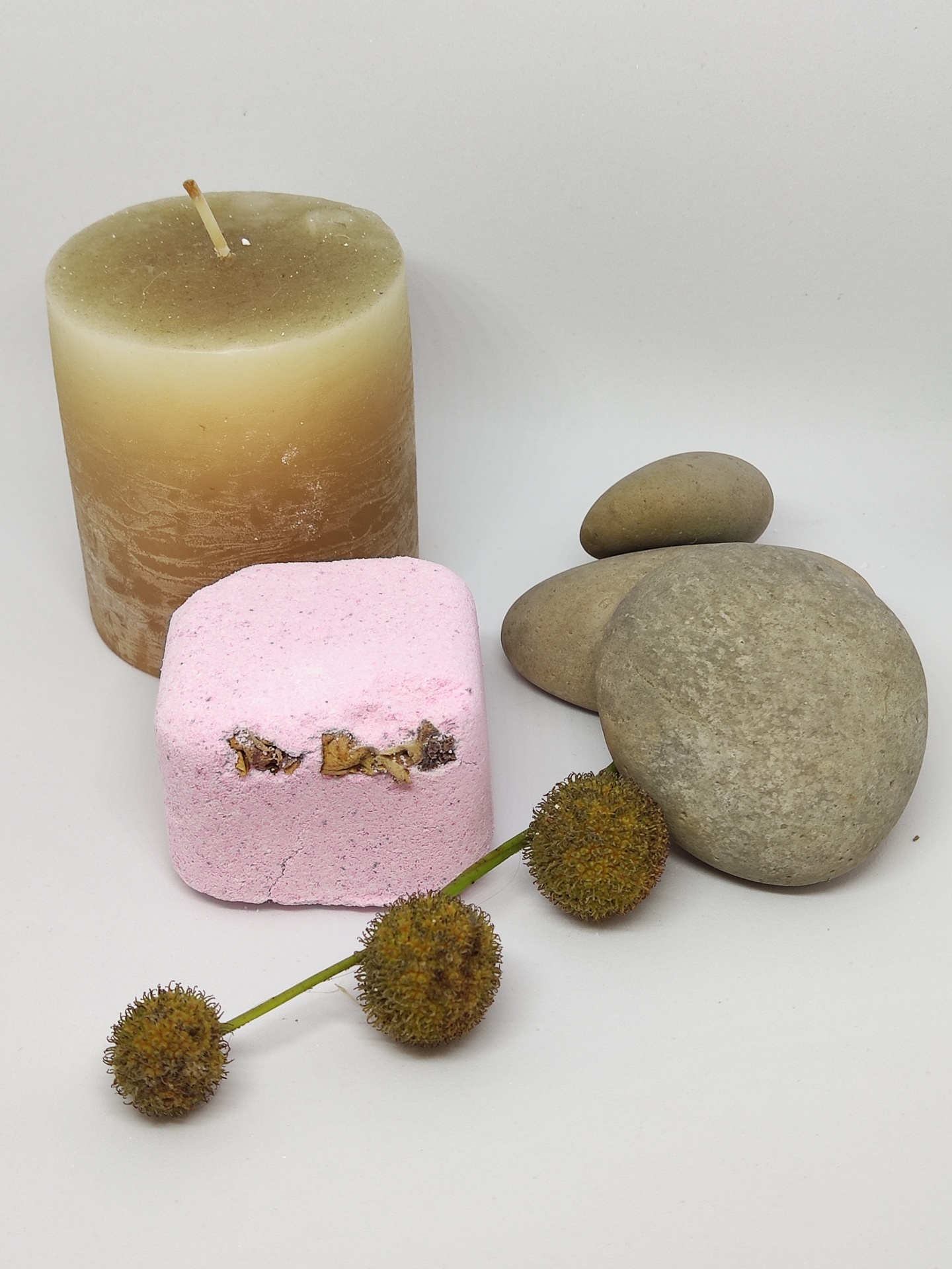 vela creme e marrom, cubo rosa, pedras cinza e ramo com sementes castanhas