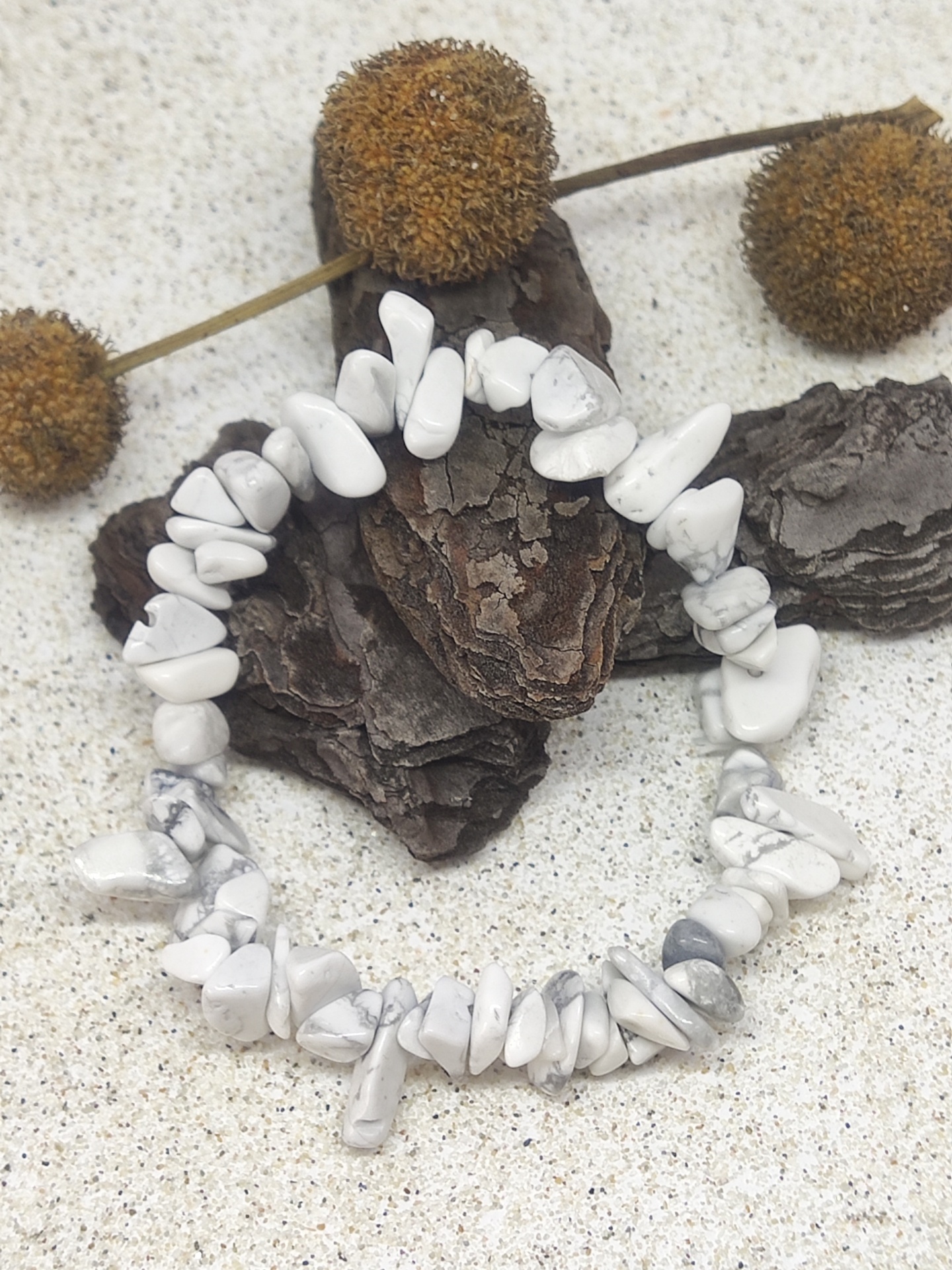 Pulseira elástica com pedras howlite brancas e cinzentas sobre casca de árvore e flores secas