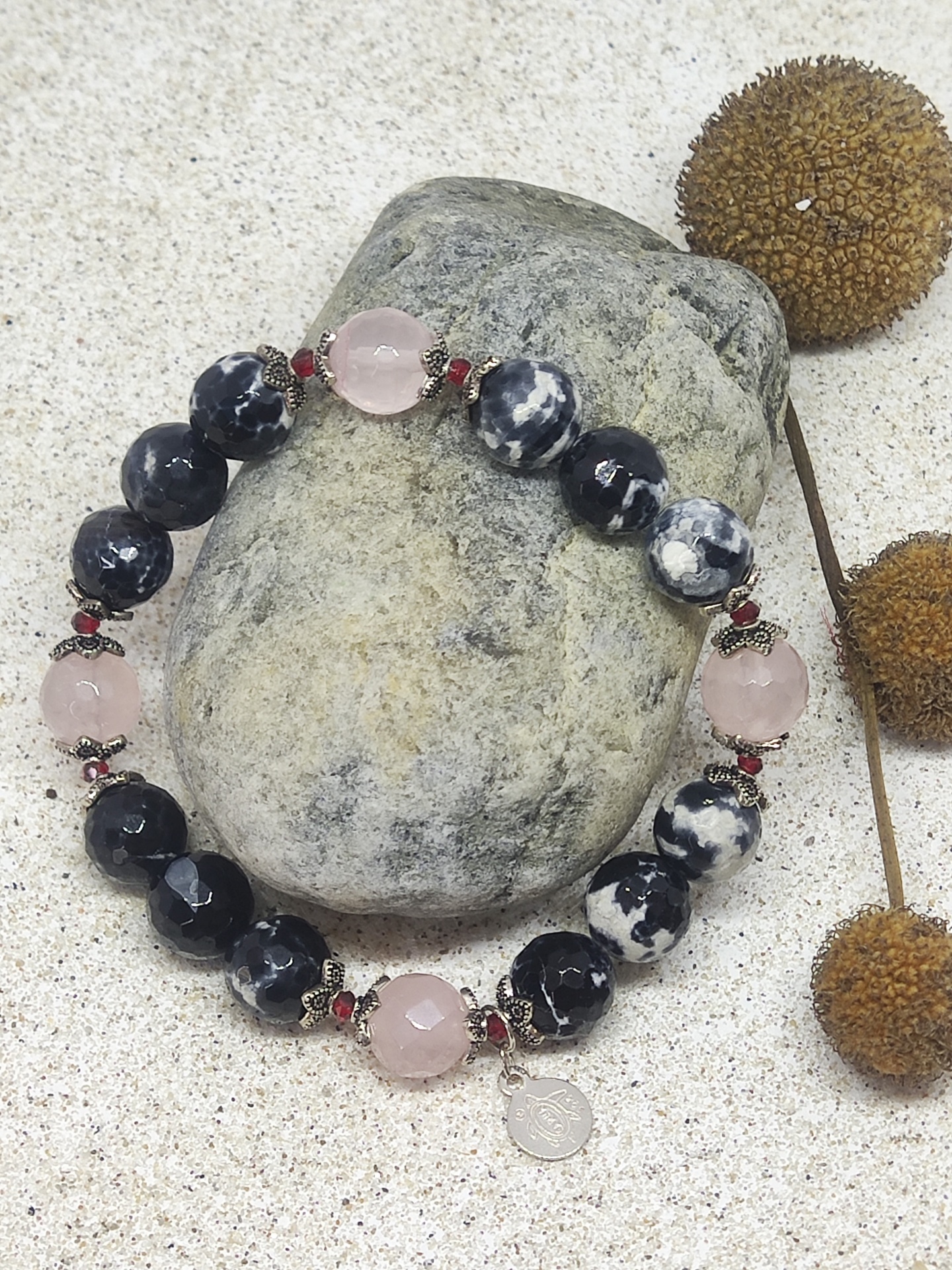Pulseira de contas pretas, brancas e rosa com pendente prateado sobre pedra cinza