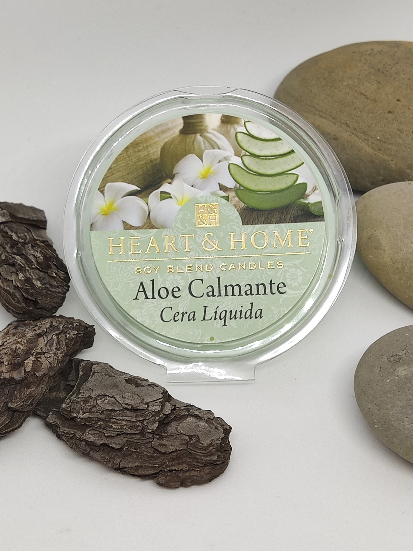 Vela de cera líquida Aloe Calmante da Heart & Home com flores e aloe vera, rodeada por pedras e casca