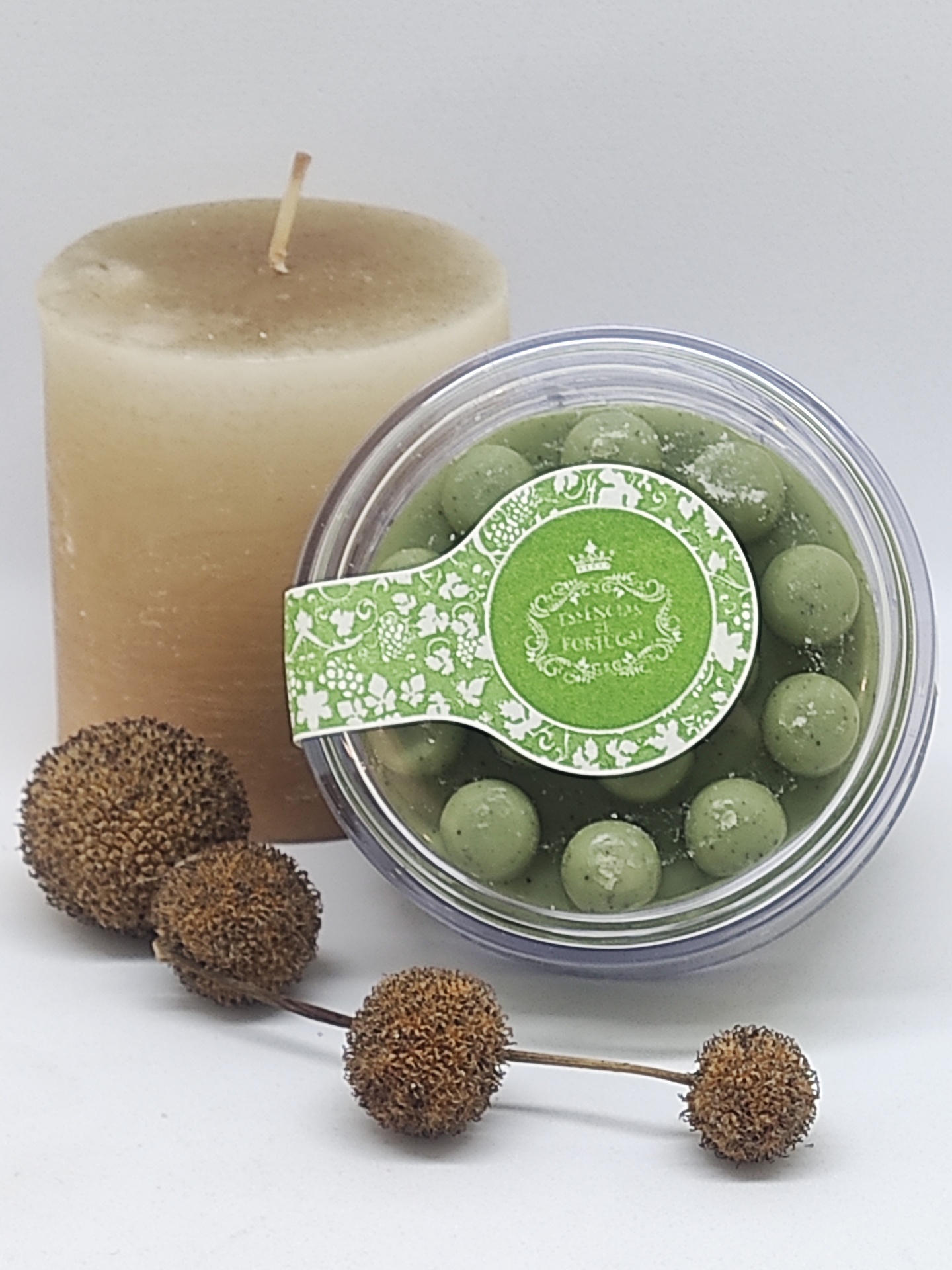 Vela bege, caixa com bolas verdes decorativas e galho de frutos secos secos