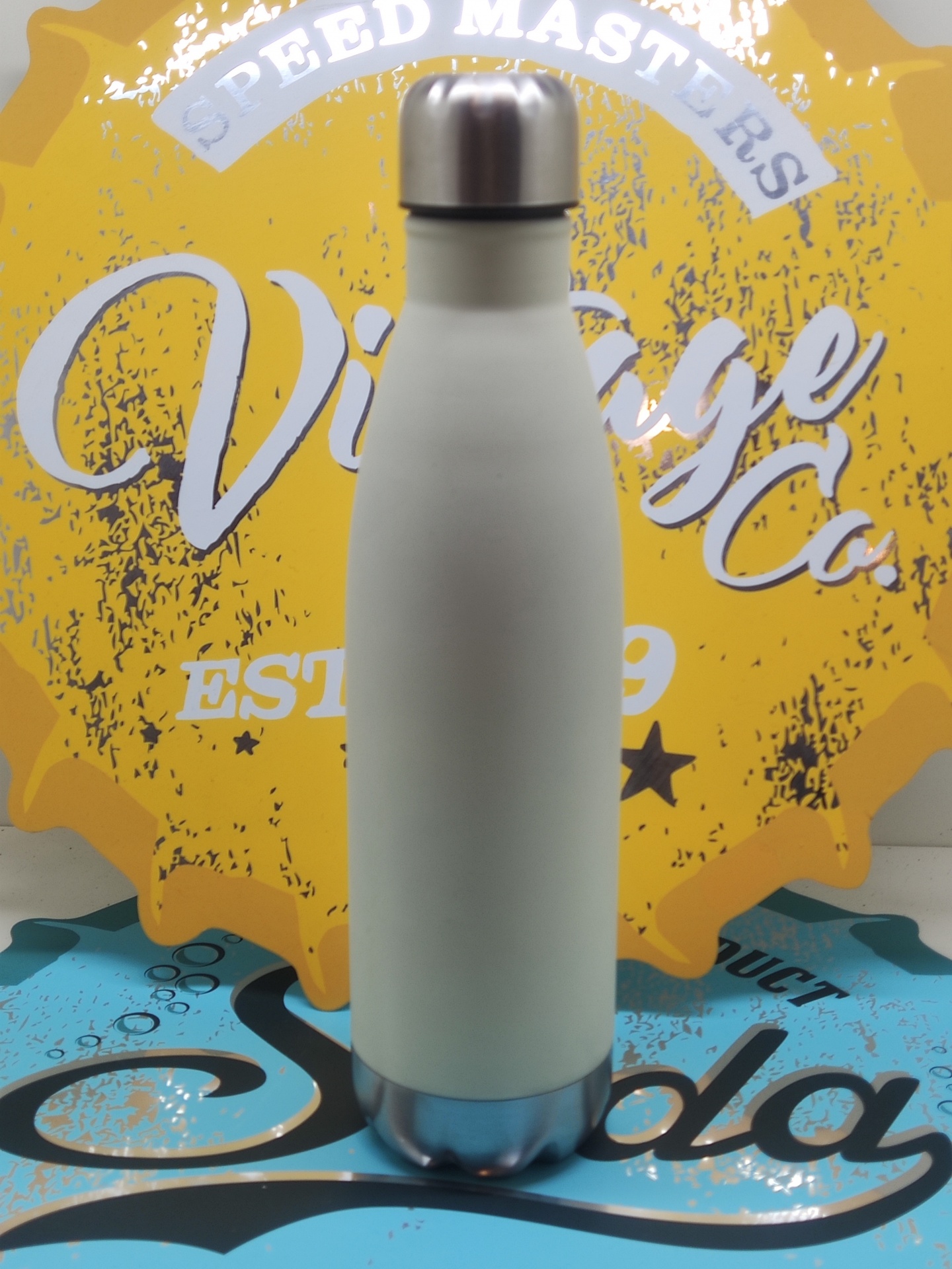 Garrafa térmica branca com tampa e base de aço inoxidável contra fundo amarelo e azul com texto vintage