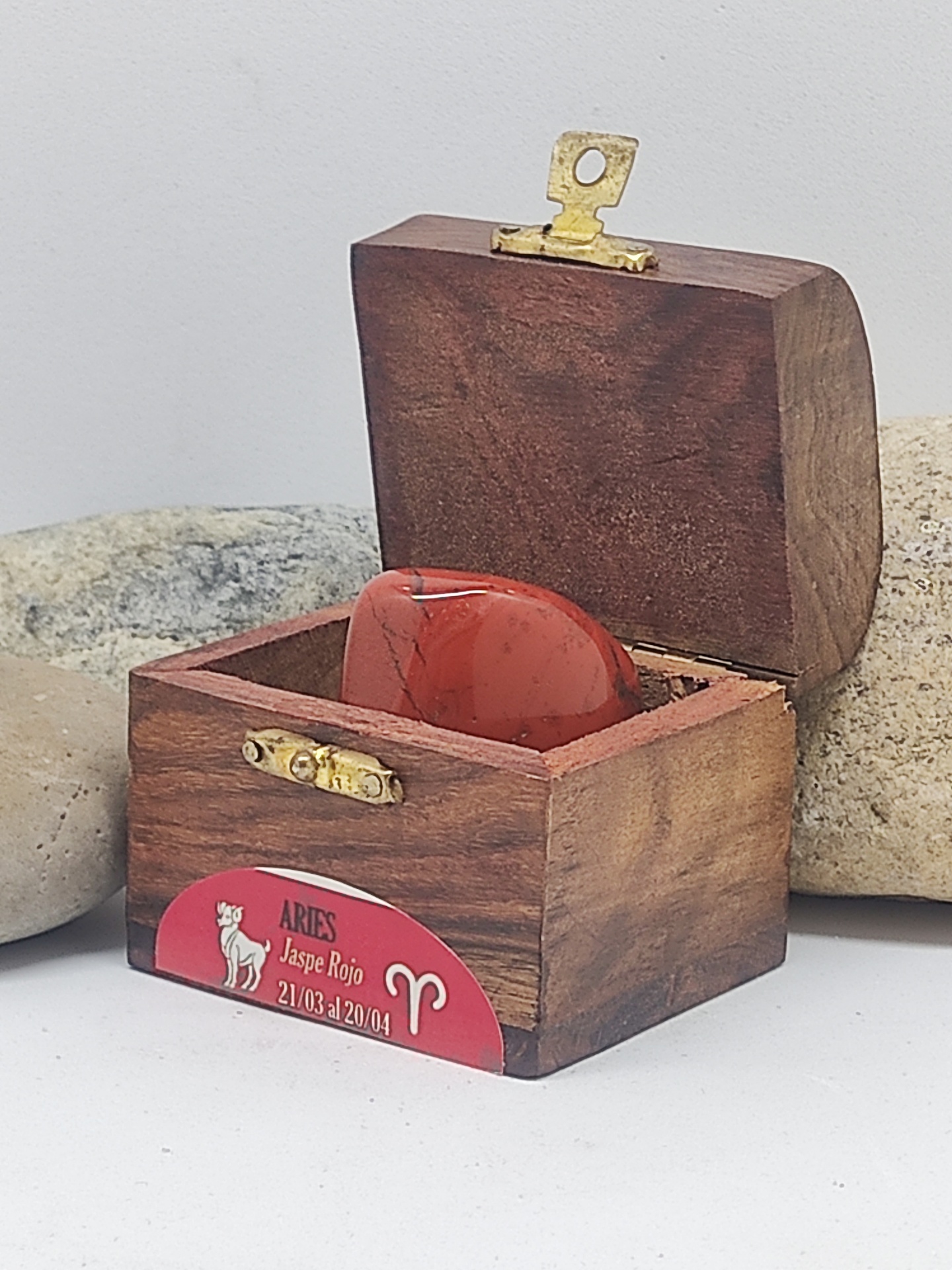 Caixa de madeira aberta com pedra vermelha e etiqueta Aries Jaspe Rojo.