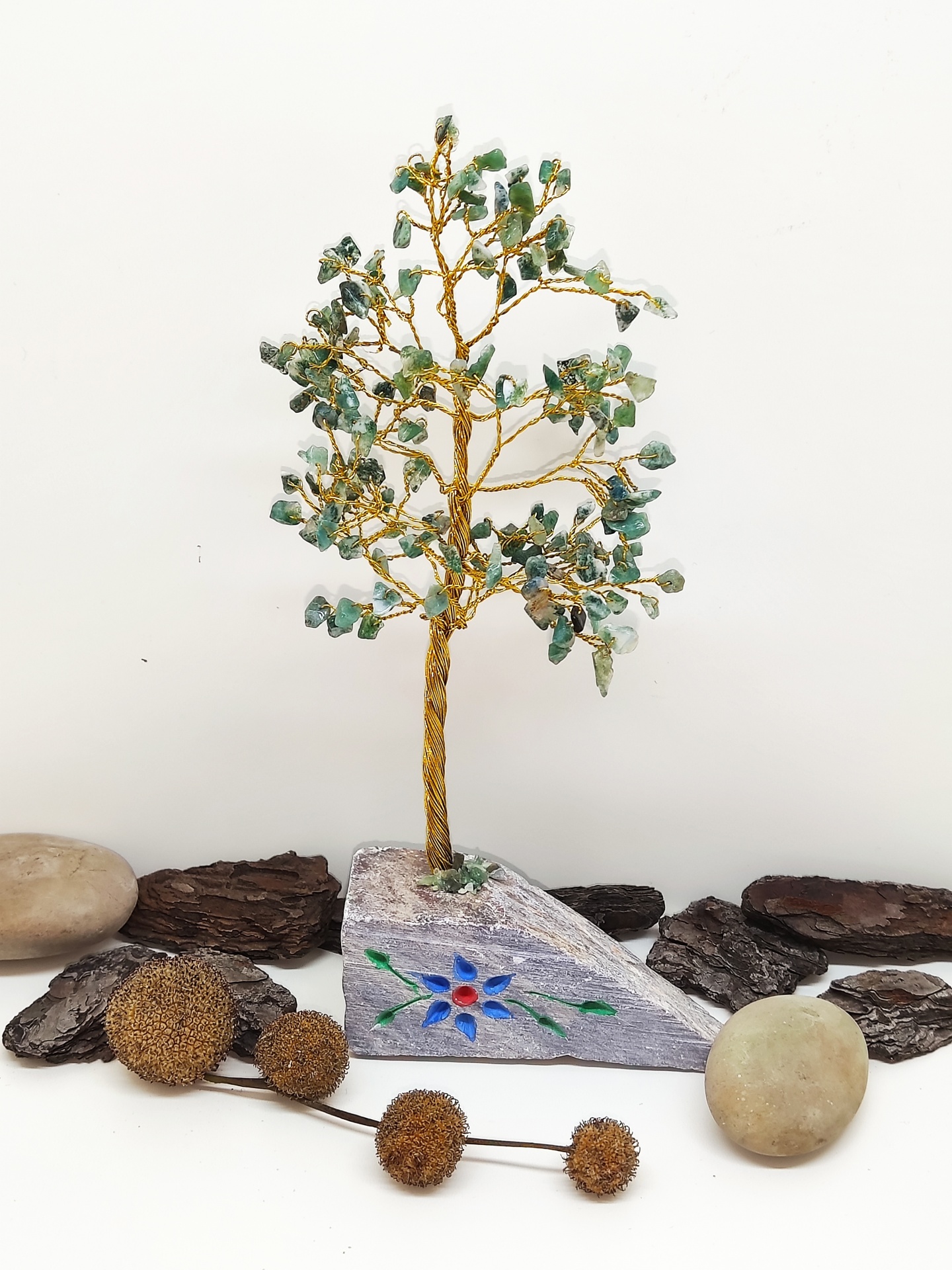 Árvore decorativa de arame dourado e pedras verdes em base com desenho floral e pedras ao redor