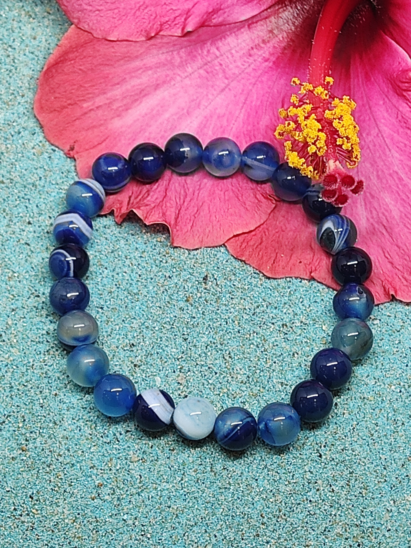 Pulseira de pedras azuis com flor rosa ao fundo sobre superfície azul