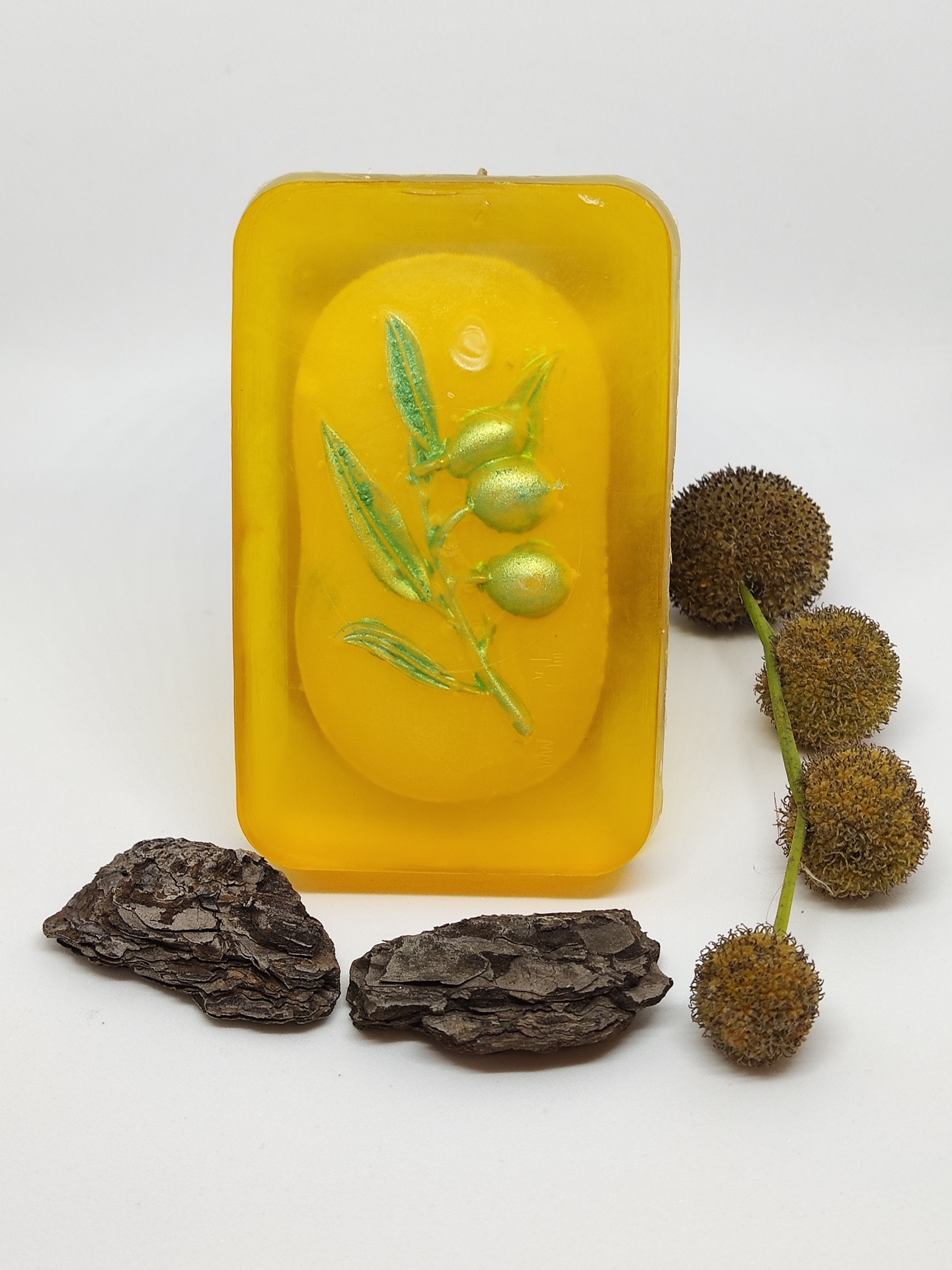 Sabonete amarelo com ramo verde e frutos dourados, casca de árvore escura e frutos peludos marrons