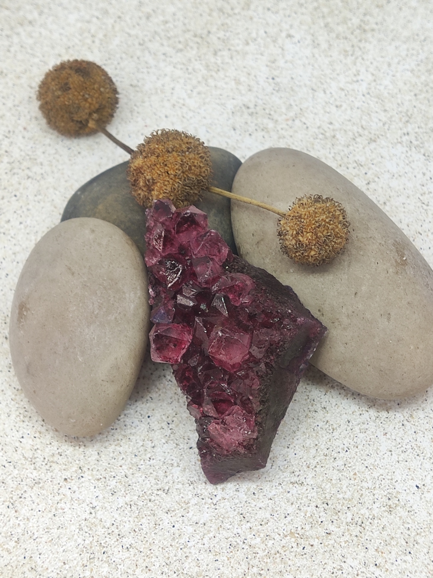 Pedra mineral com cristais roxos sobre pedras lisas e botões secos