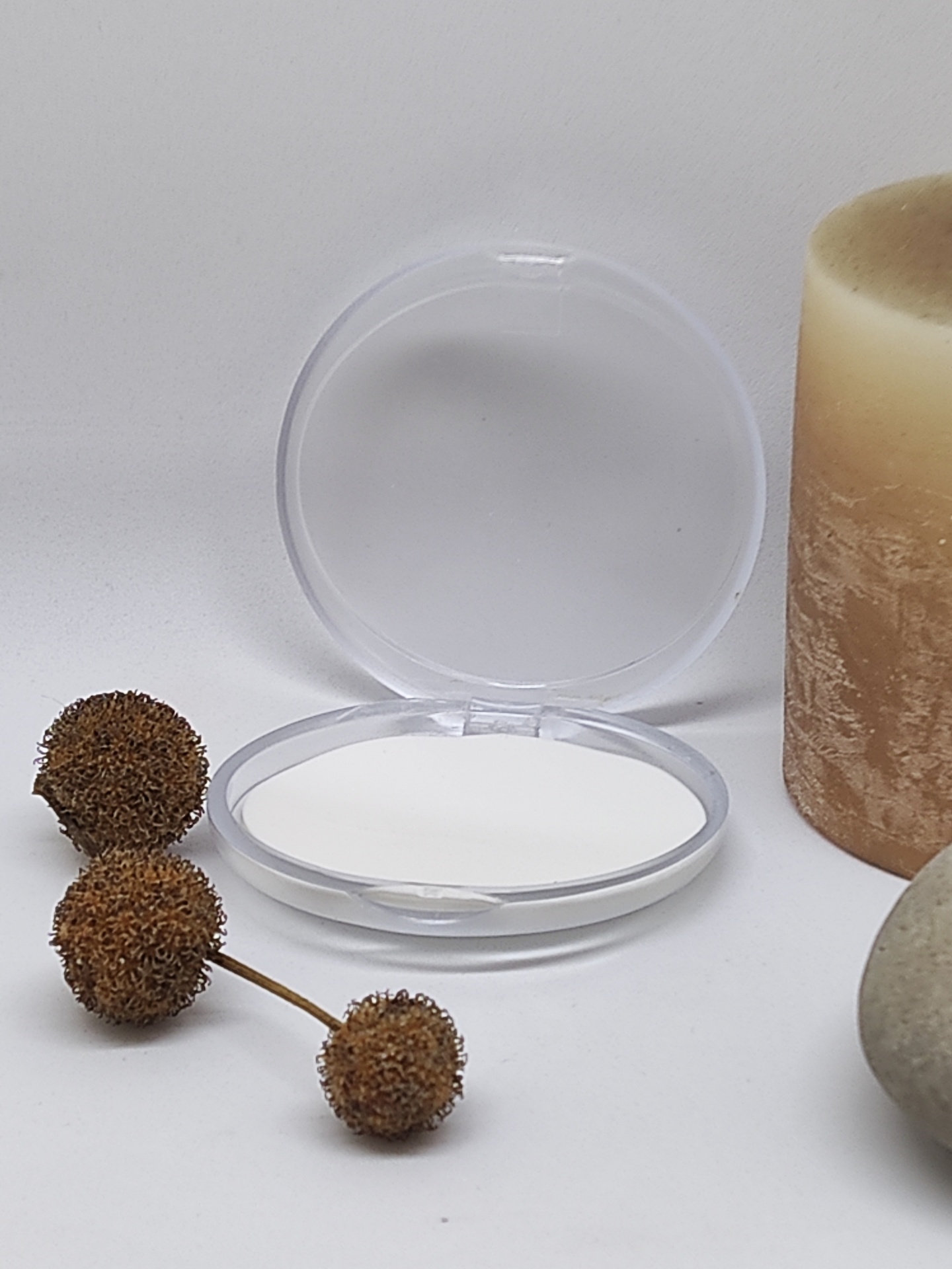 Espelho redondo aberto com tampa transparente junto a vela castanha e bagas secas