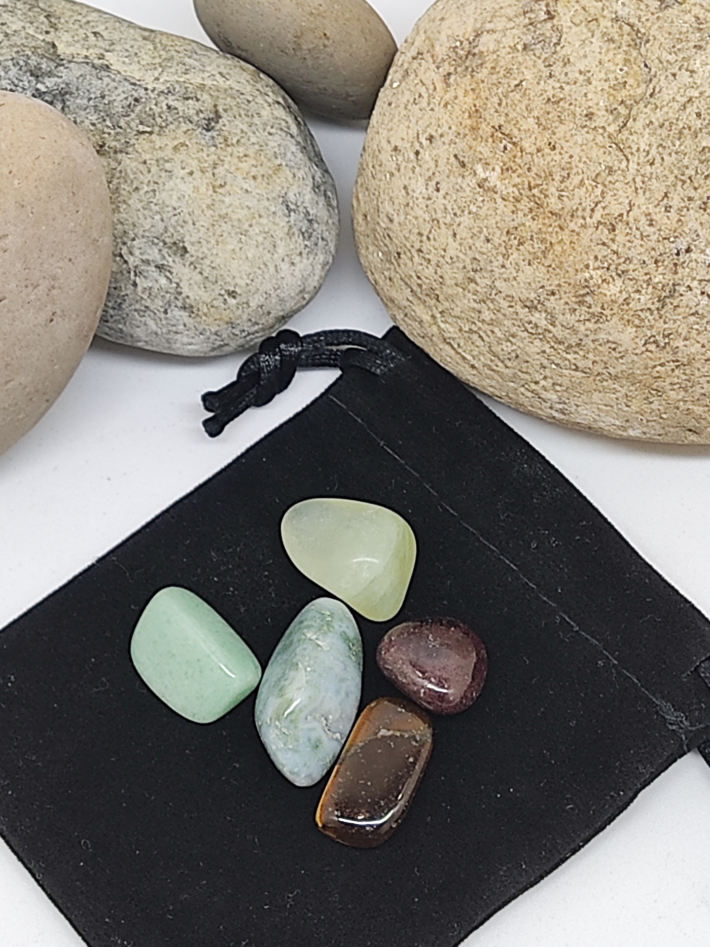 Cinco pedras polidas coloridas sobre saco de tecido preto, rodeadas por pedras maiores