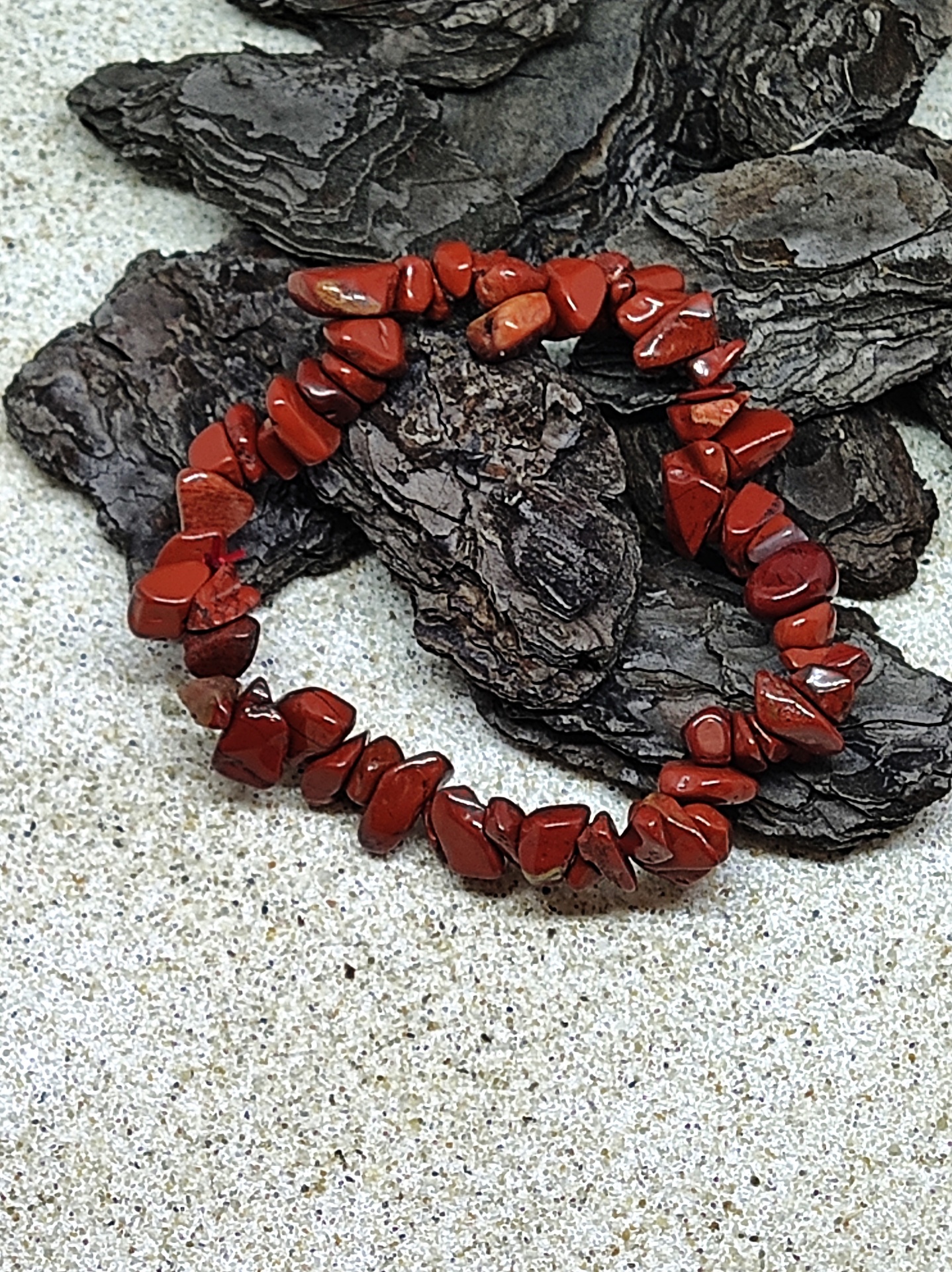 Pulseira de pedras vermelhas sobre casca de árvore e superfície clara