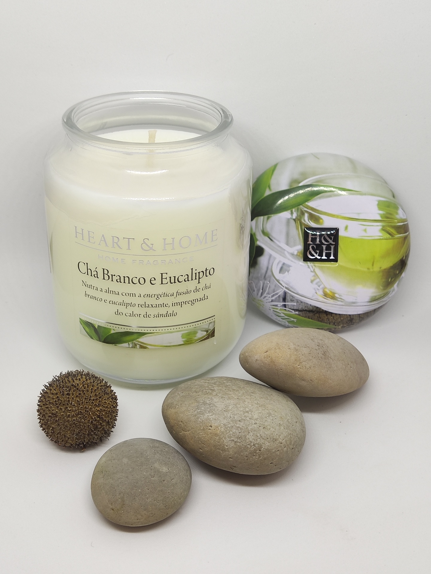 Vela aromática em vidro com tampa decorada, pedras lisas e bola texturizada.