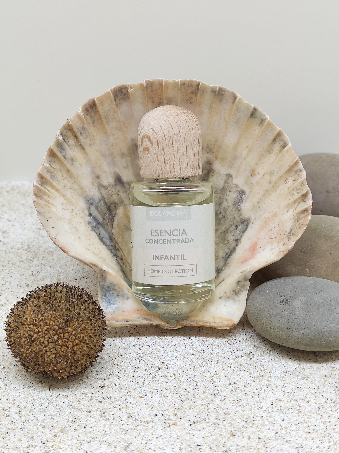 Frasco de essência infantil em concha marinha sobre areia com pedras e semente