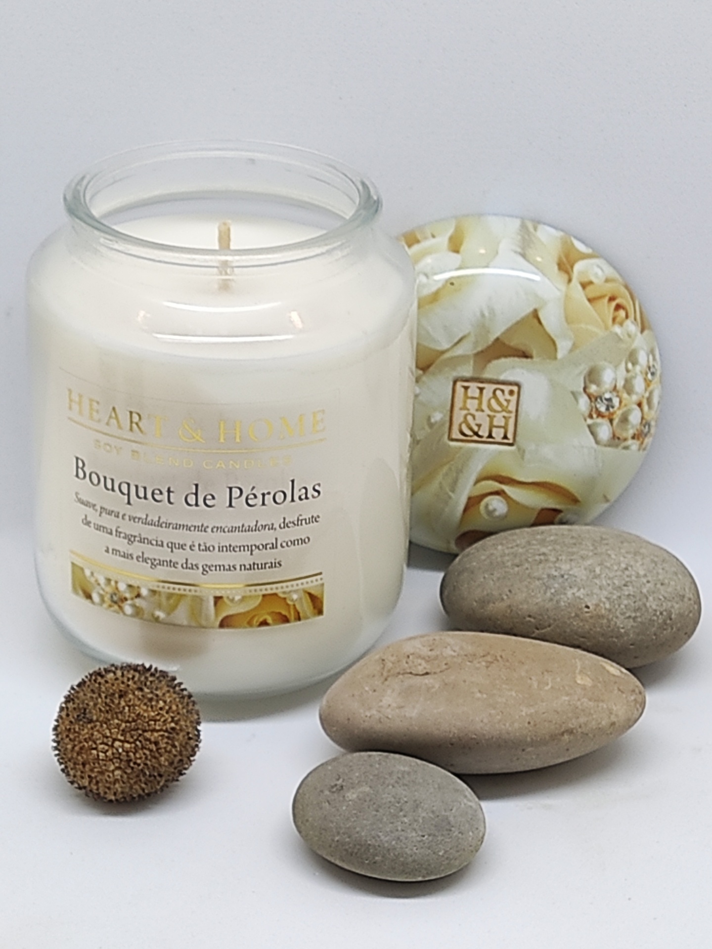 Vela em vidro branco com tampa decorativa e pedras lisas ao lado