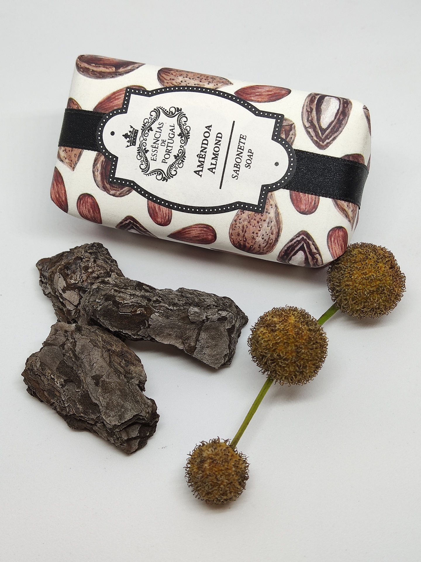 Sabonete de amêndoa embalado com padrão de amêndoas e rótulo branco e preto, casca de árvore e ramo com bolas secas castanhas