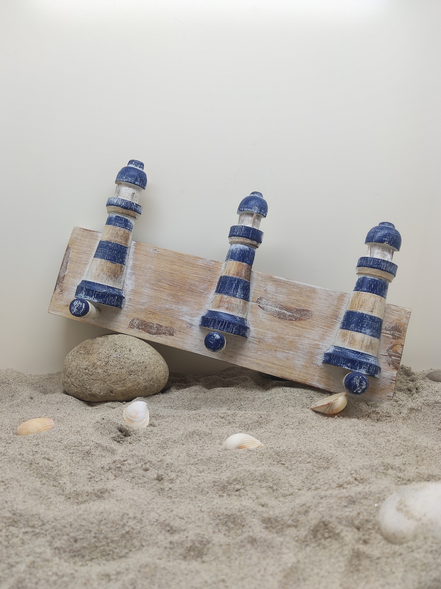 Cabide decorativo de faróis azuis e brancos na areia com pedras e conchas