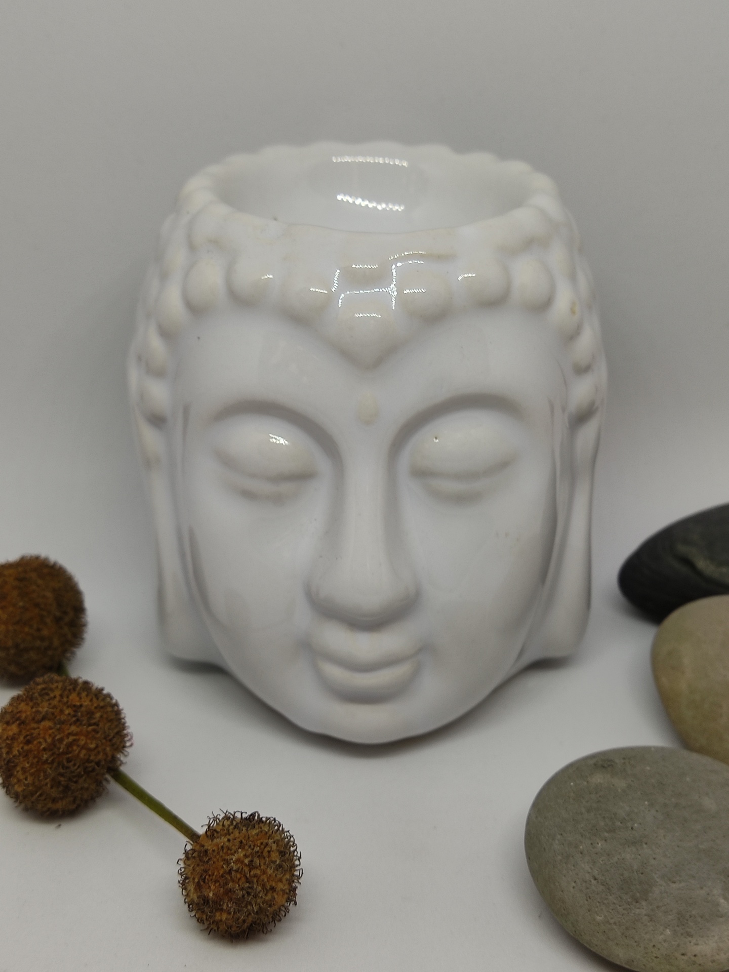 Vaso cerâmico branco em forma de cabeça de Buda com pedras e raminhos secos ao redor