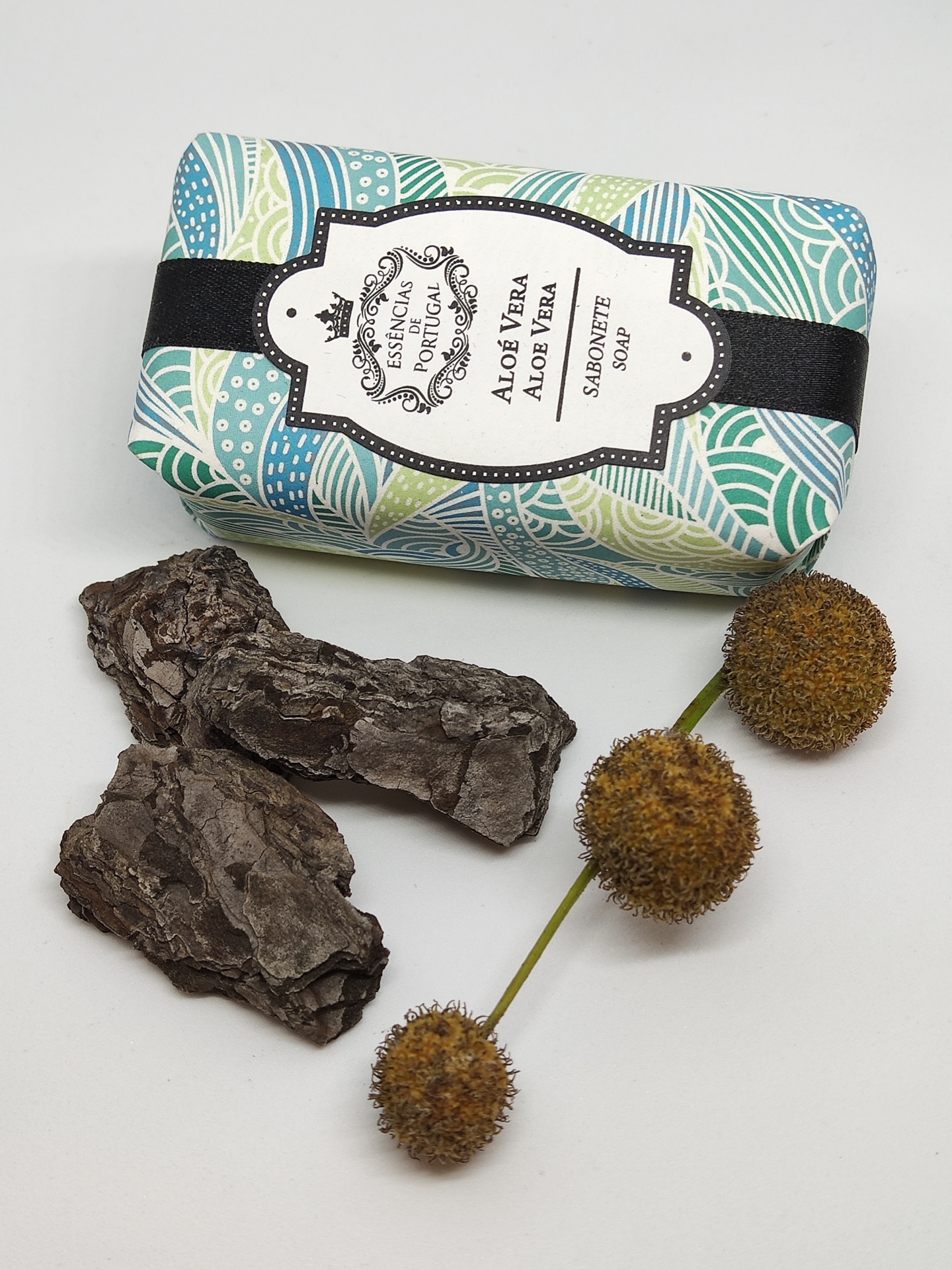 Sabonete Aloe Vera embalado com papel padrão colorido ao lado de cascas e bolas secas marrons.