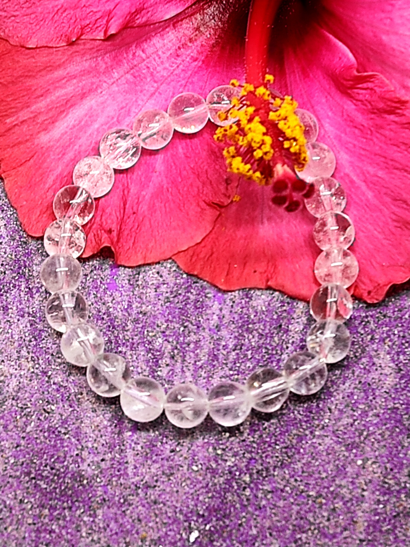 Pulseira transparente sobre superfície roxa com flor rosa