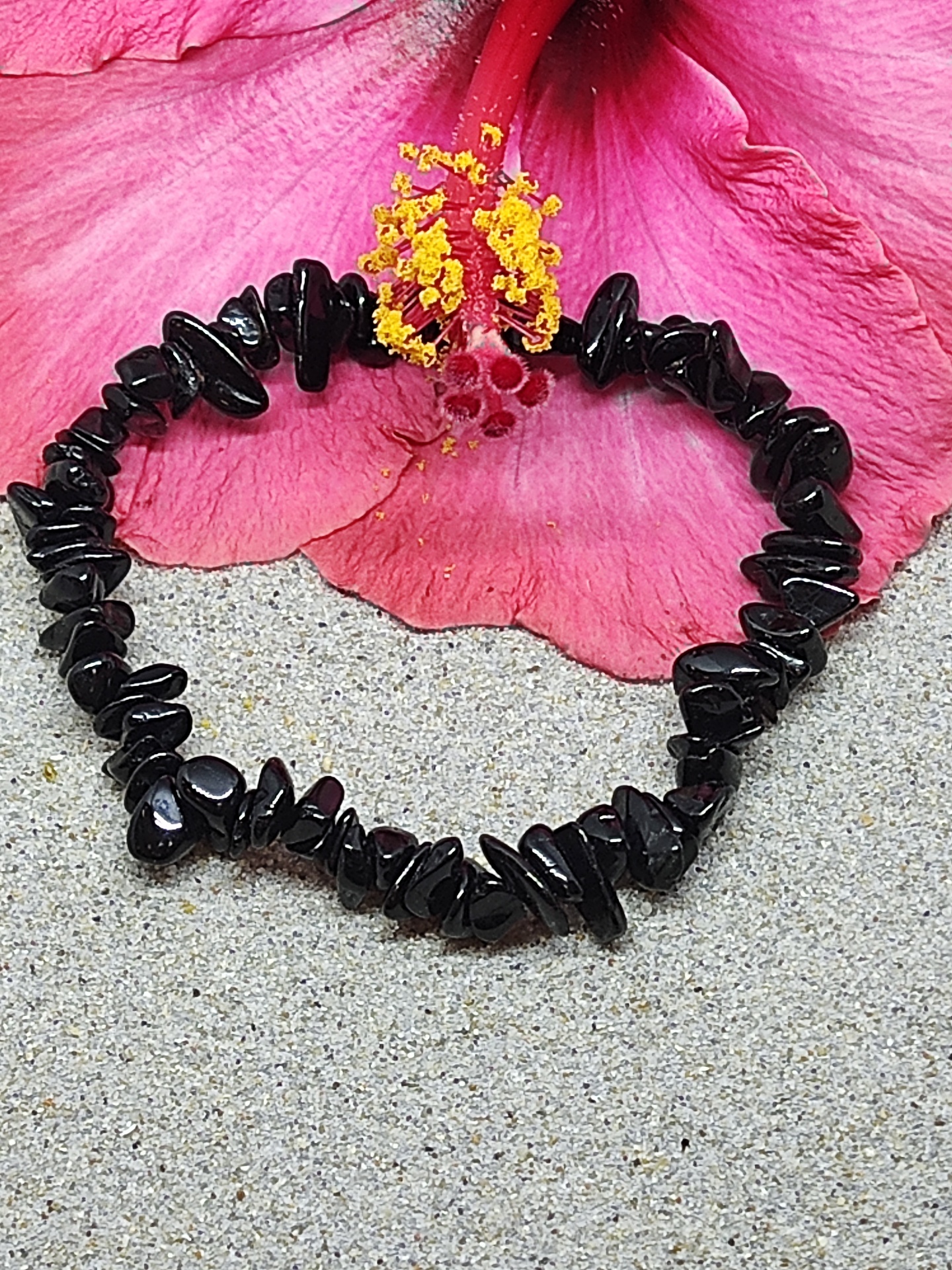 Pulseira de pedras negras irregulares com flor rosa e amarela ao fundo