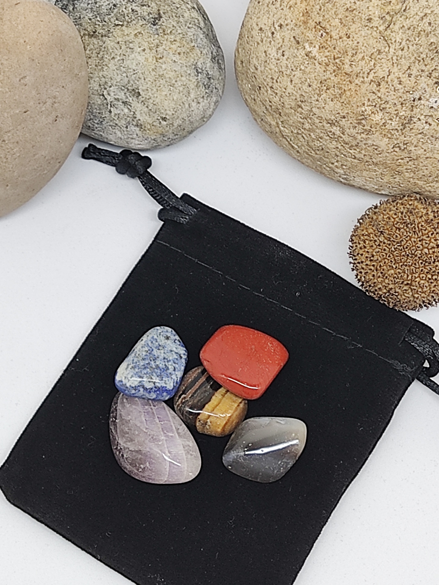 Cinco pedras polidas coloridas em saco preto de veludo rodeadas por pedras naturais maiores e ouriço do mar