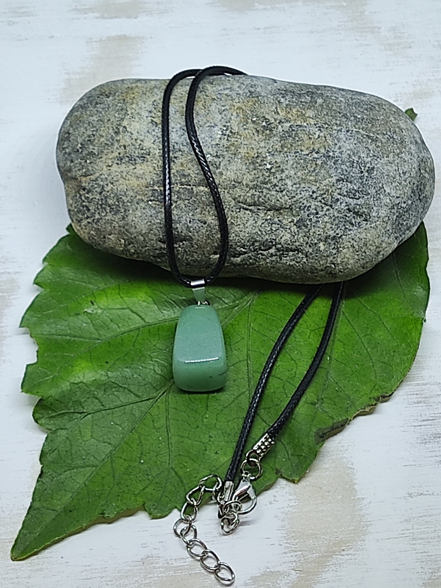 Colar com pendente verde e cordão preto sobre folha e pedra